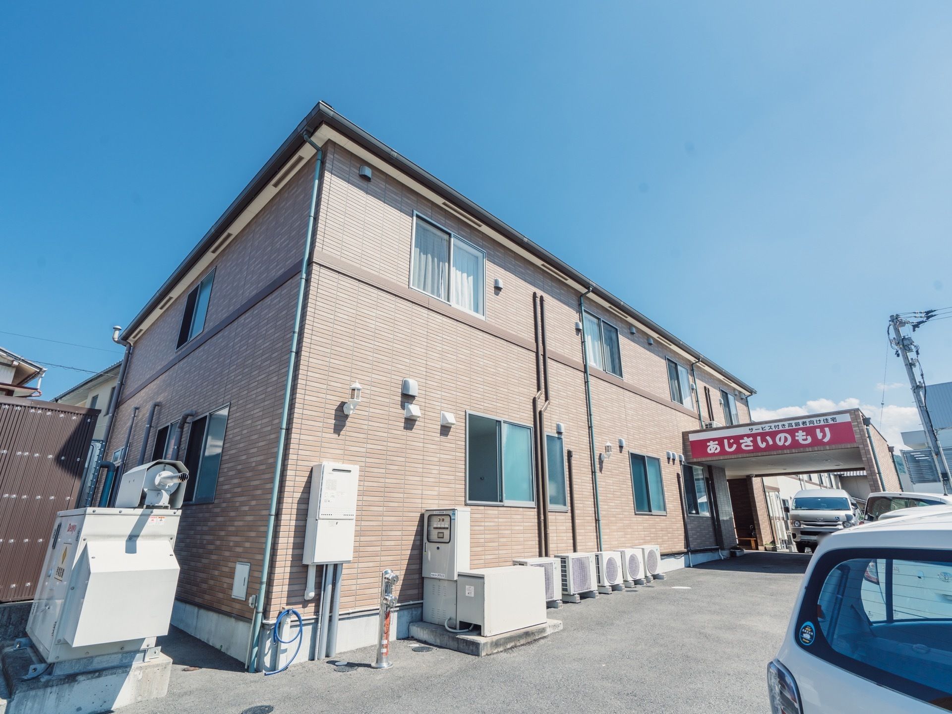 ブラウン色の外壁の２階建ての建物になっている。車を停めることができるスペースを備えており、車で来訪する際も安心である。