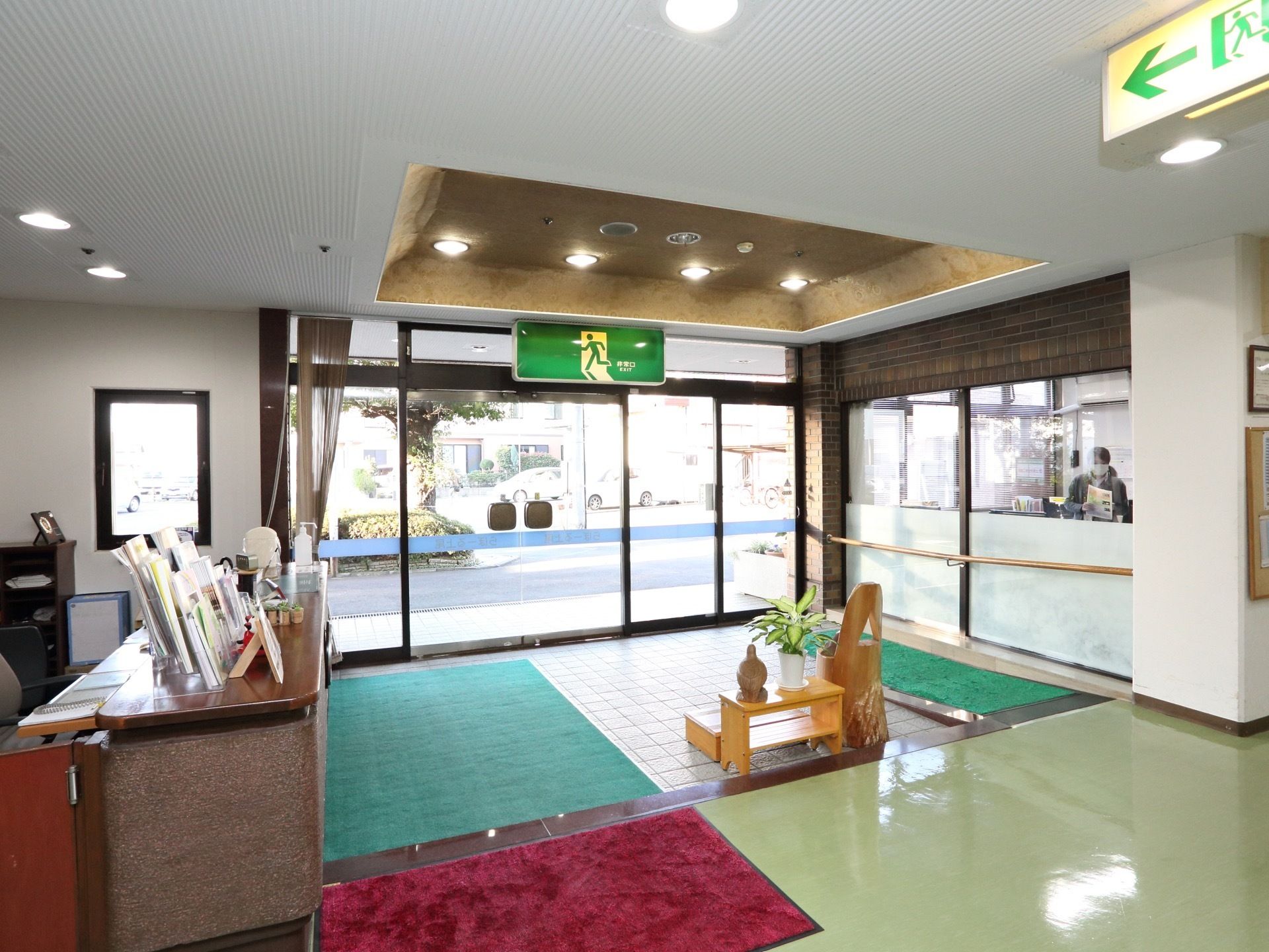 明るい玄関はガラス張りになっており、大きな緑色の非常口の案内が設置されている。スロープと手すりが設置されており、安全に移動することができる。