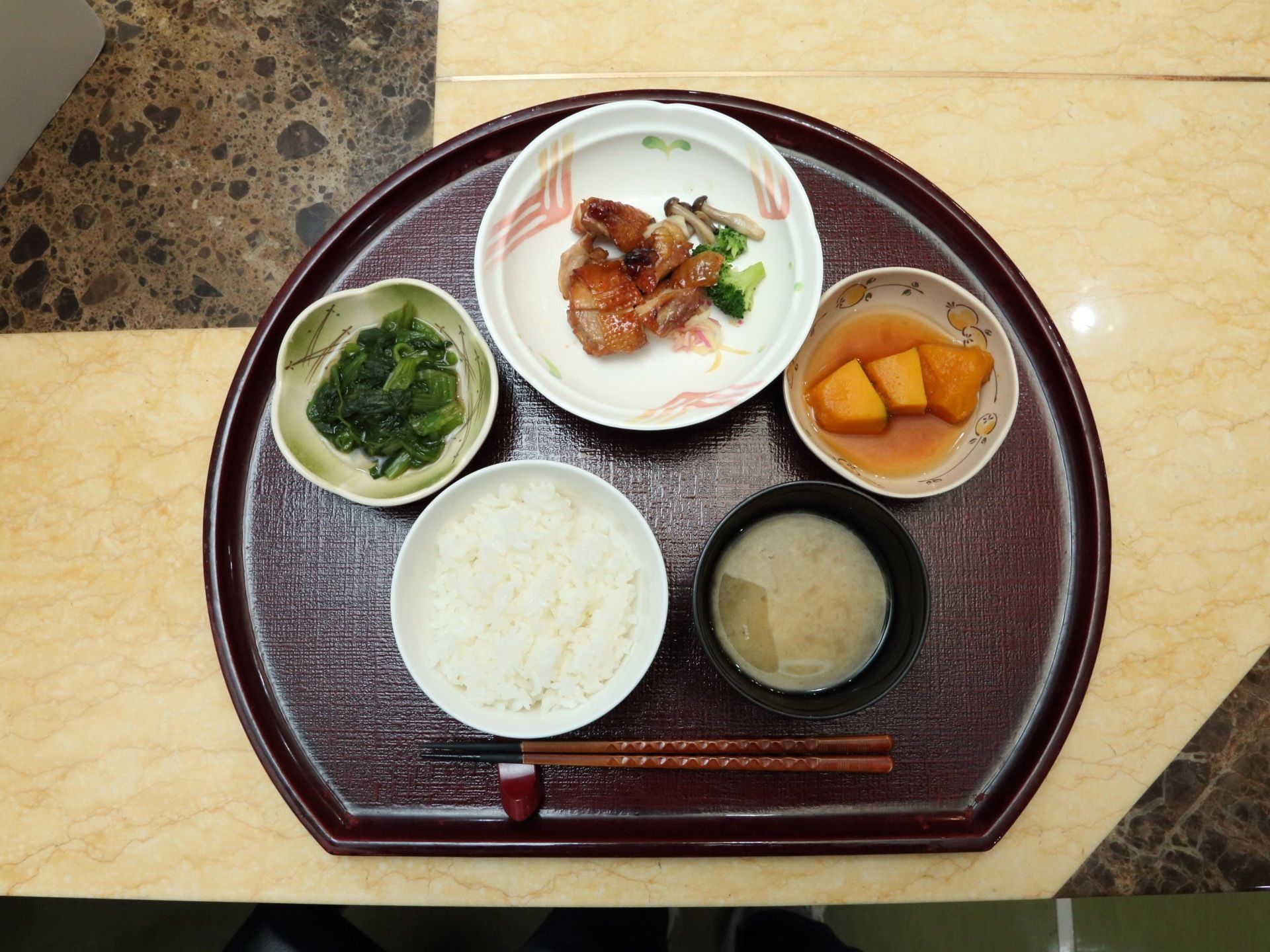 施設で提供している食事メニューの一例である。野菜を多く使った料理を彩りよく盛り付け、1人分ずつトレーに並べている。