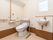 白ベースの空間にブラウンの巾木を施工し、清潔感のあるトイレである。壁には縦横に、便器の脇にも手すりを設けている。手洗いスペースもある。