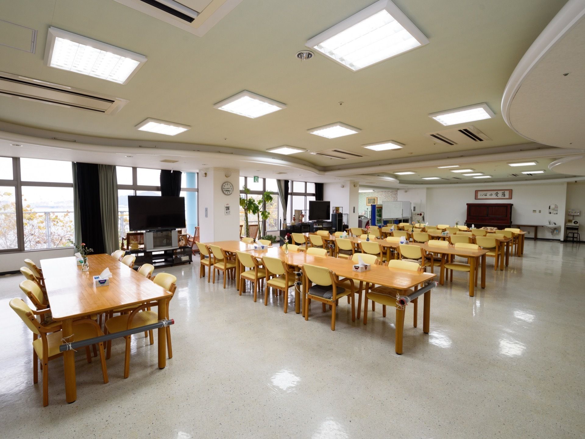 縦に4人掛けの机が並べてあり、それが4列ある。テレビが2台ある。その後ろは一面窓になっている。机の間隔が広くなっている。