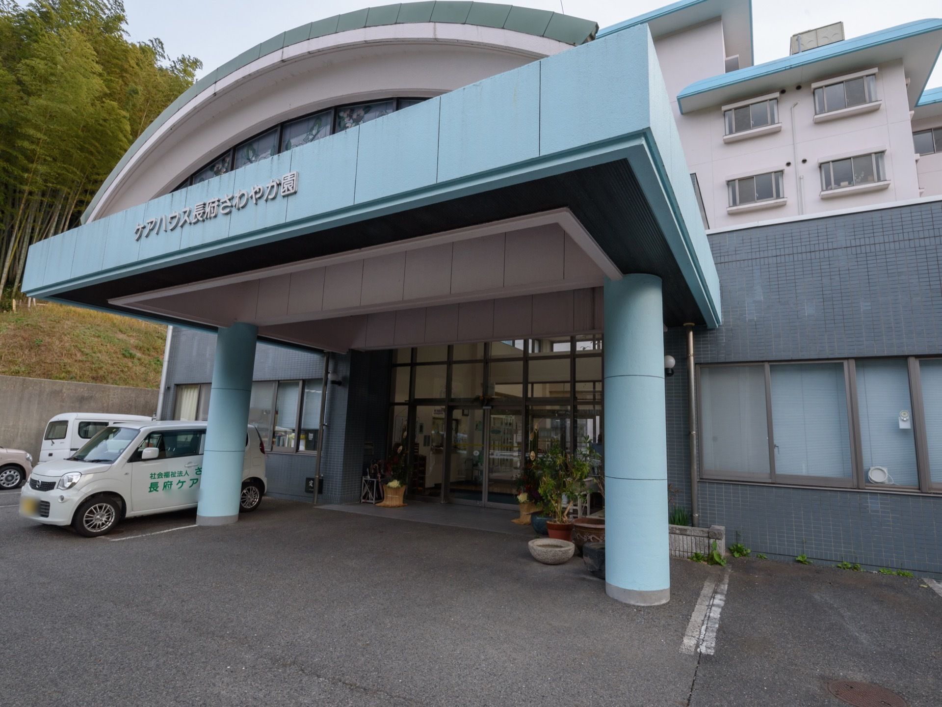 自動ドアの入り口であり、周りには観葉植物がおいてある。ドアの前は屋根がついており、車が1台止まれるほどの広さである。