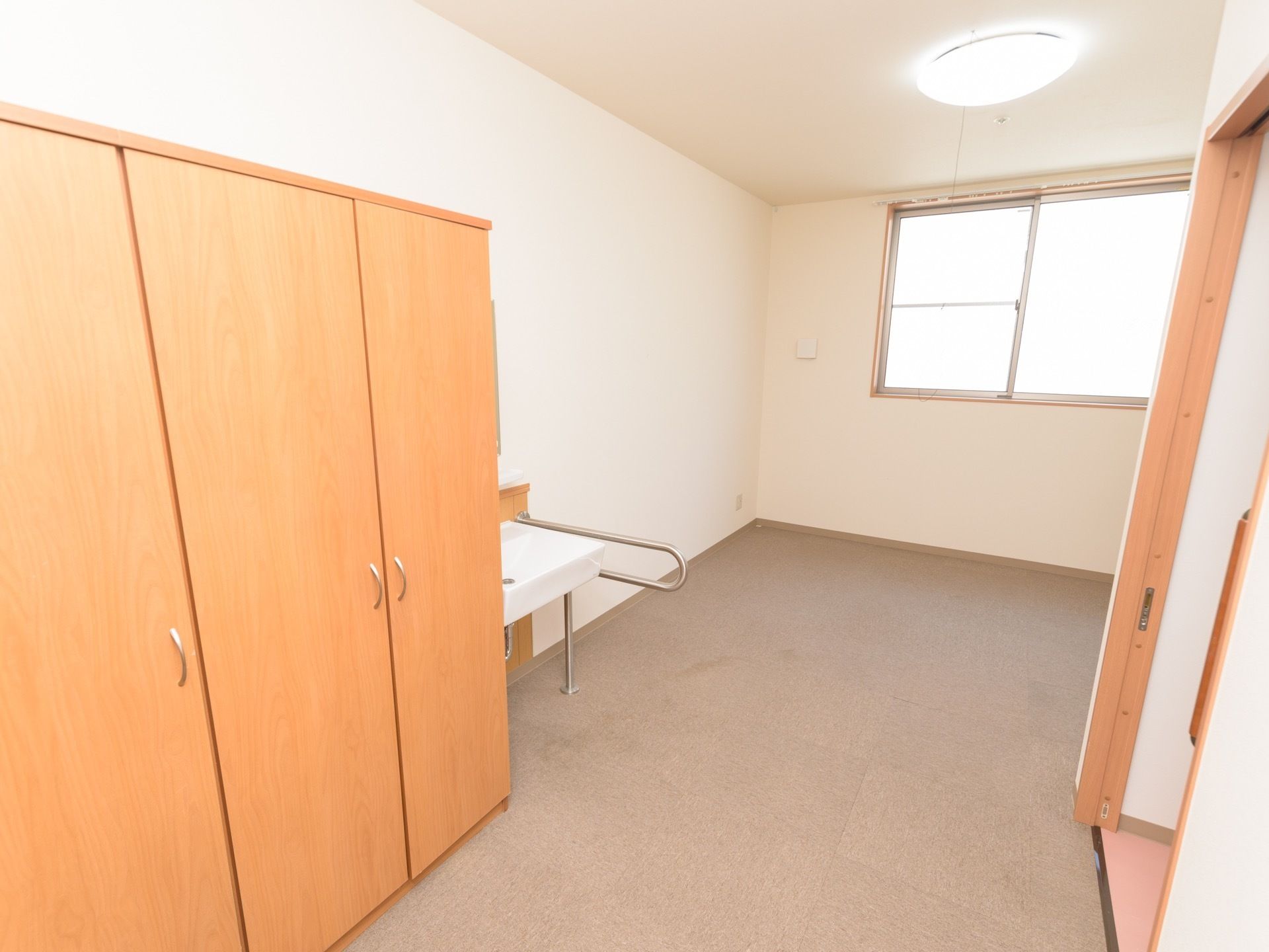 床にカーペットが敷き詰められた部屋。左側に木製の収納棚があり、その隣には洗面台が取りつけられている。
