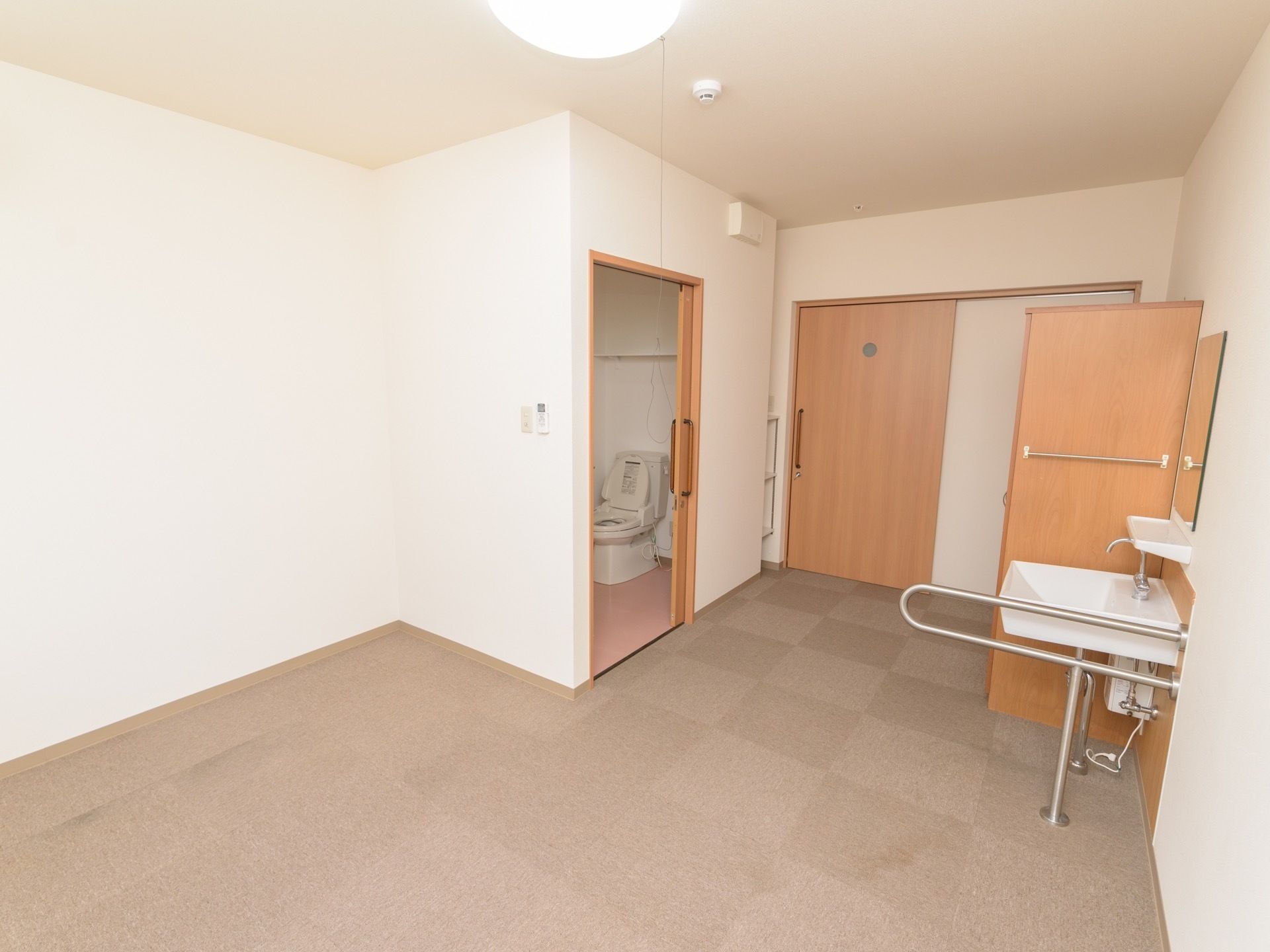 左側の引き戸が開いており、奧に洋式便器が見える。右側には、洗面台と背の高い収納家具が設置されている。