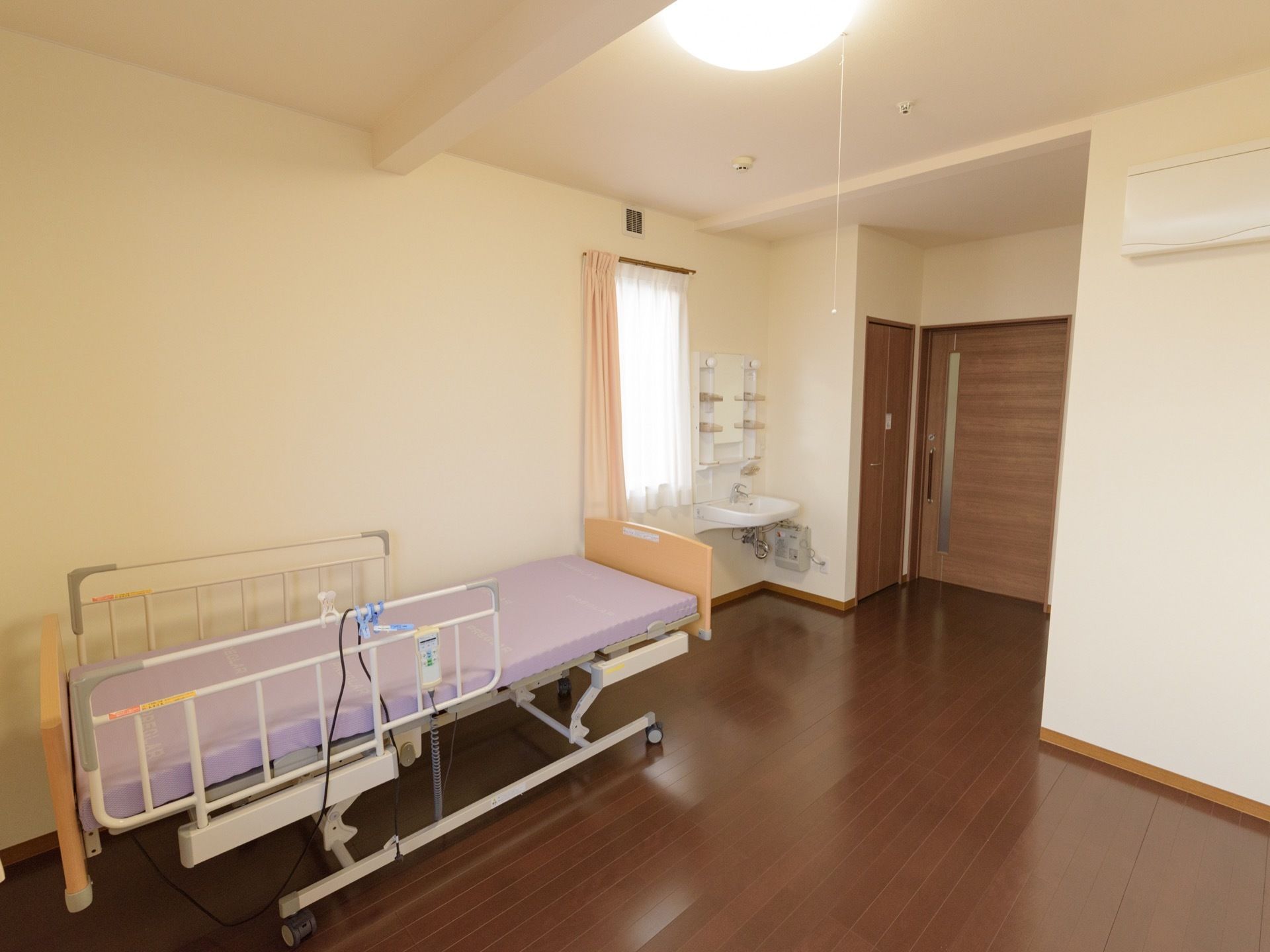 居室には介護用ベッドがある。床はフローリングで入口扉は引き戸になっている。壁際には車椅子で利用できる洗面台がある。