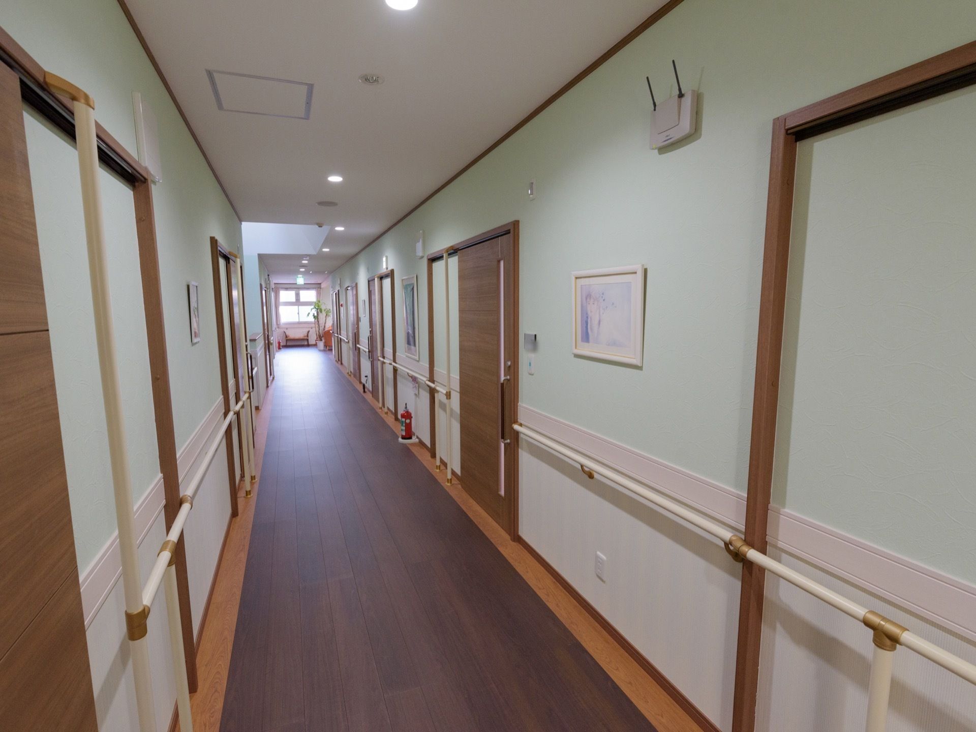 長い通路の左右に居室がある。壁には手すりがあり、居室入口の扉の所にも手すりがある。フローリングと木目調の扉が落ち着いた雰囲気になっている。