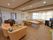 フローリングの部屋にダイニングテーブルセットとソファーやチェストが置いてある。角にはカー店の掛かったまどがある。