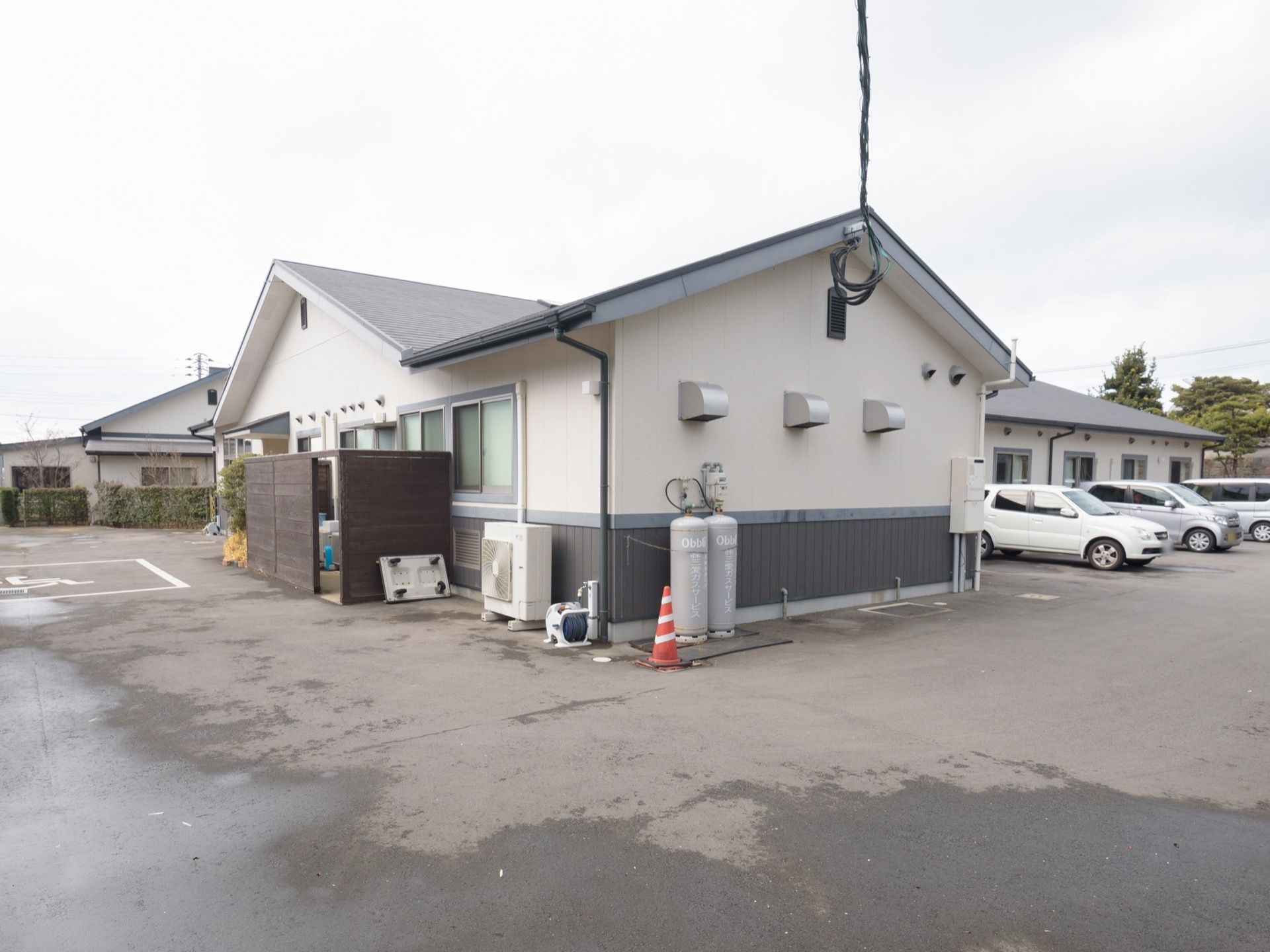広い敷地に建っている木造１階建ての施設である。建物の裏手に広い駐車スペースが設けられている。外水道が設置されている。