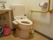 洗面台も備わったトイレである。便器には、温水洗浄便座が設置されている。L型手すりが壁に取り付けられている。