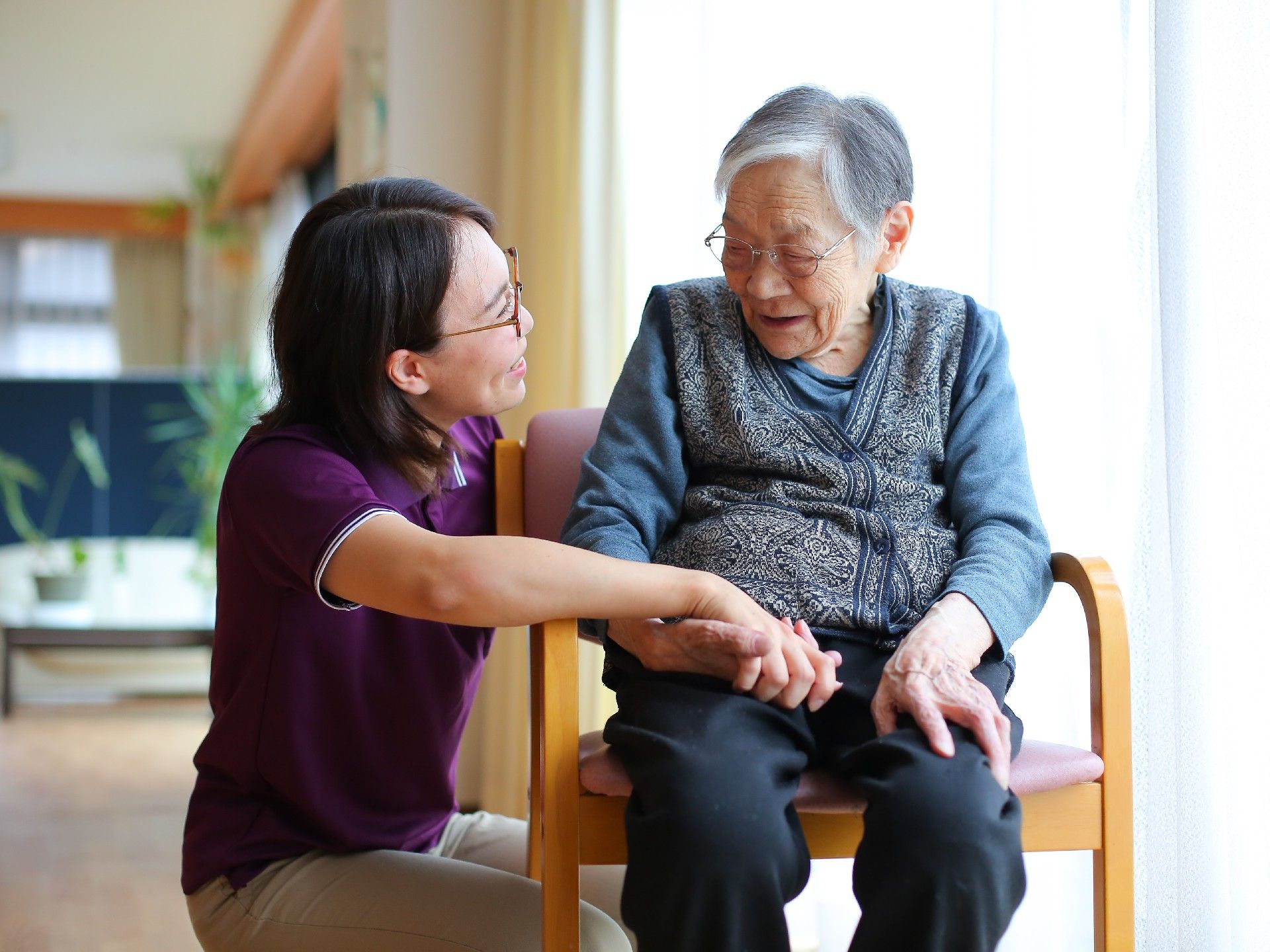 女性スタッフが利用者の手をにぎりながら、笑顔で会話をしている