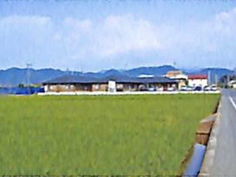 道路脇に青々と広がる畑を前面に立地している平屋建ての施設外観