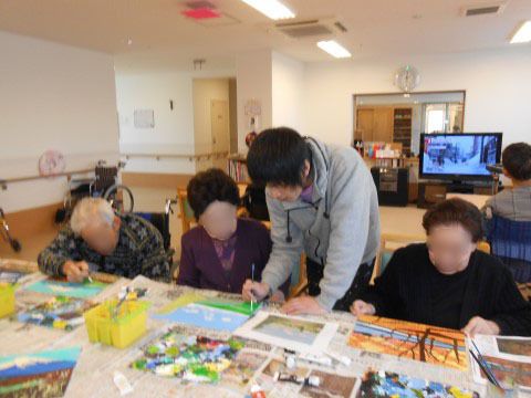 レクリエーションで模写の仕方を入居者様に助言する１名の男性スタッフ