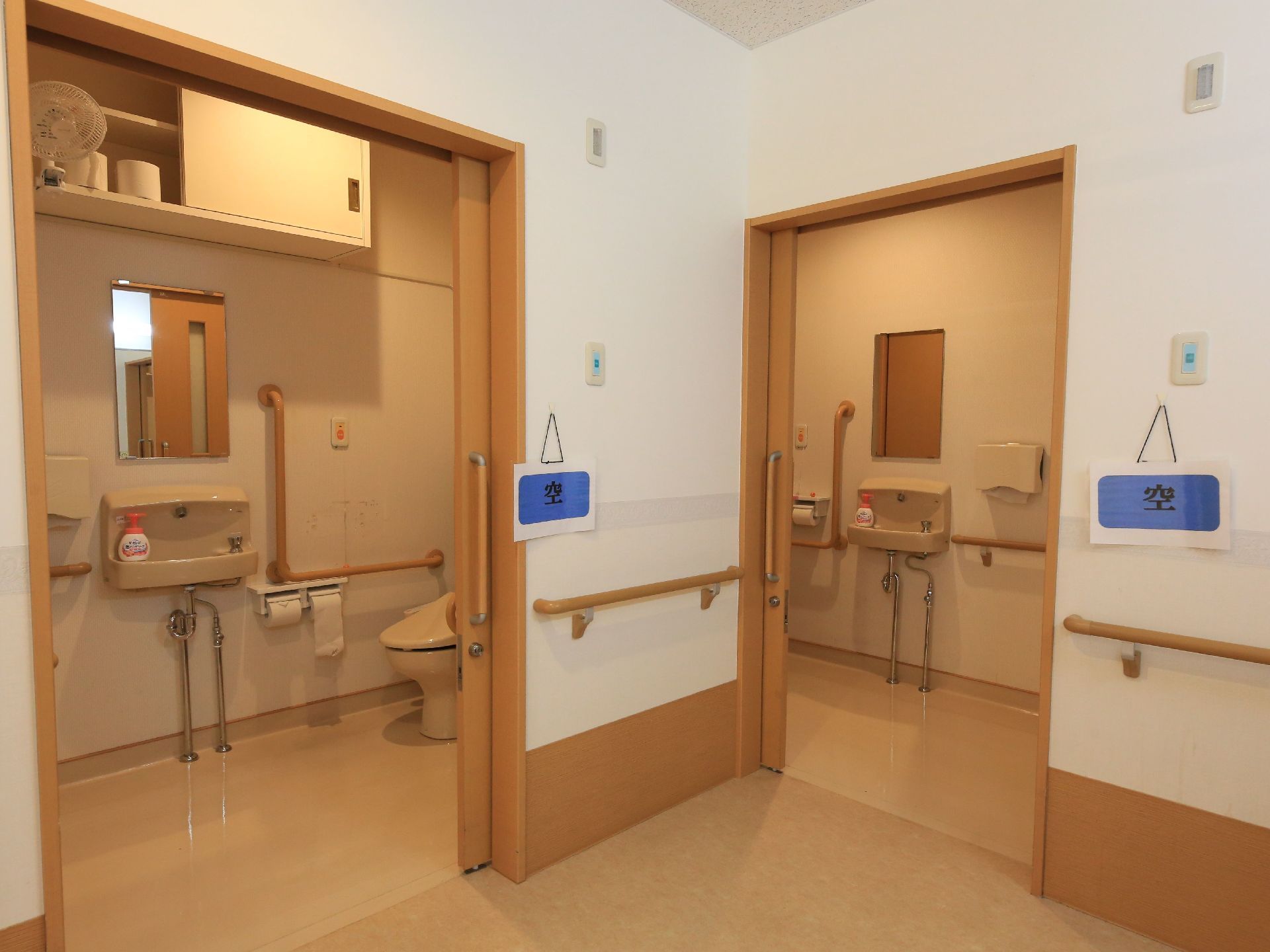 上部にトイレットペーパーなどが入っている収納棚がある。洋式便座の近くの壁にL字型の手すりが設置されている。