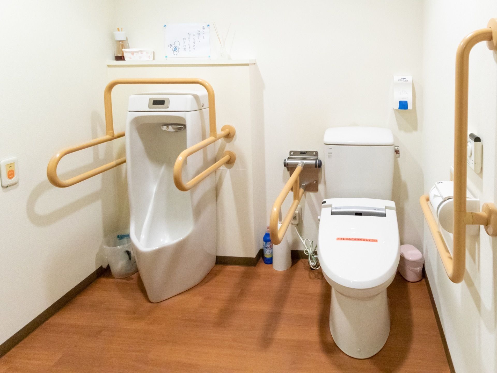 トイレには男性用の便器にも洋式便座の周囲にも手すりがかかっている。便器の周りのスペースが広く取られている。