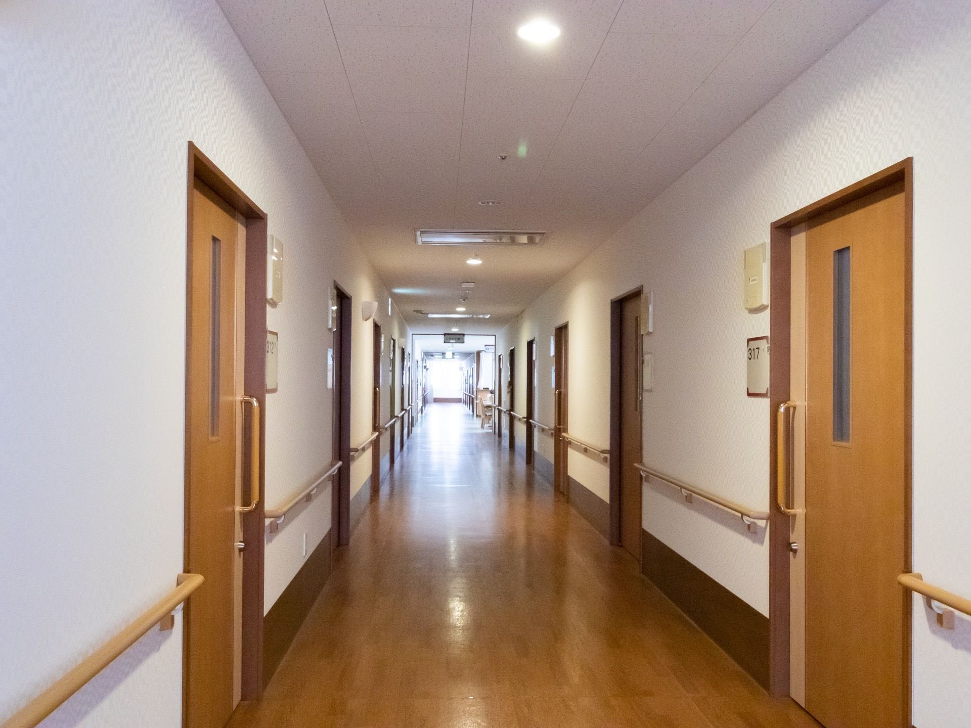 通路の床と居室の扉、手すりの色が同じ系統で、統一感がある。通路の幅はゆったりとしている。両サイドに手すりがある。