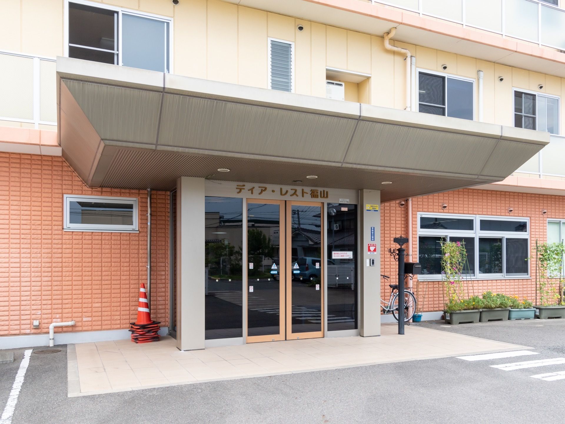 施設の外観は、イエローとオレンジ色のツートンカラーである。玄関にはポーチがあり、自動ドアの上に施設名の表示がある。
