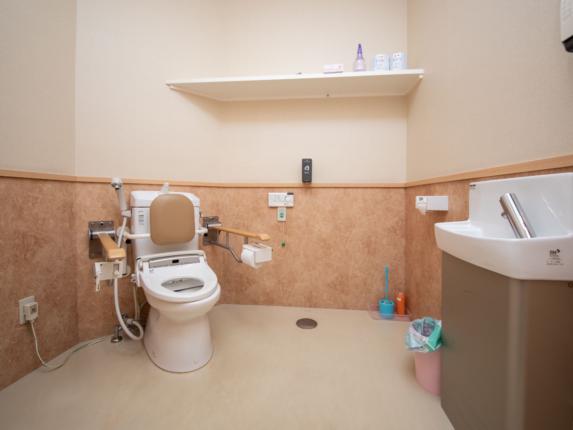 車椅子をご利用の方がスムーズに利用することができる広いトイレである。便器には可動式の肘掛けや背もたれが設置されている。