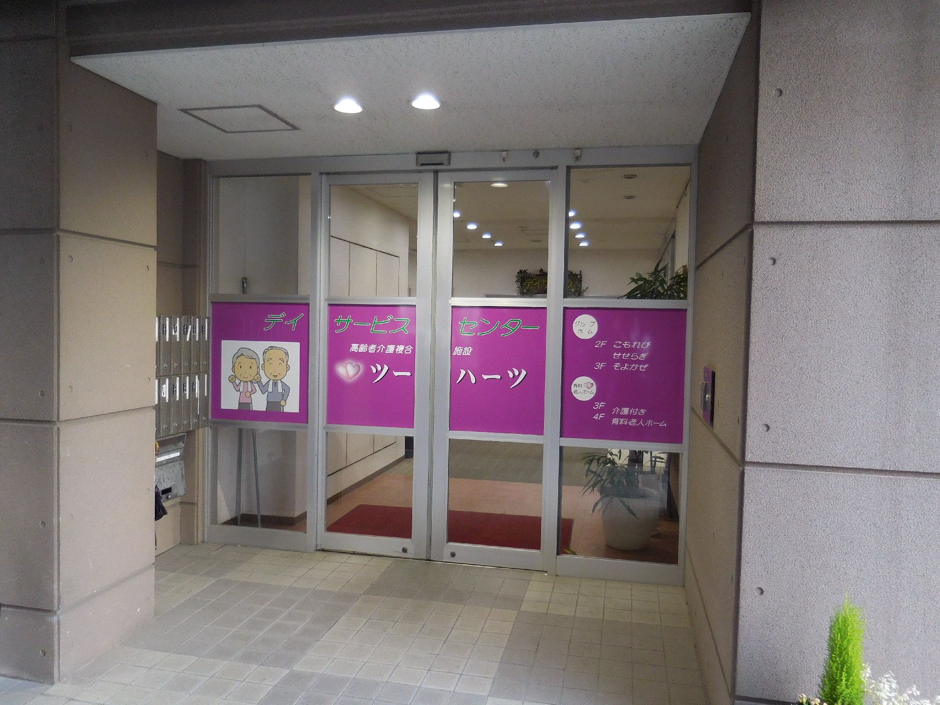 玄関は中央から両開きするタイプの自動ドアになっている。ドアには施設名とロゴが大きく記載されている。ドアの横には郵便ポストが設置されている。