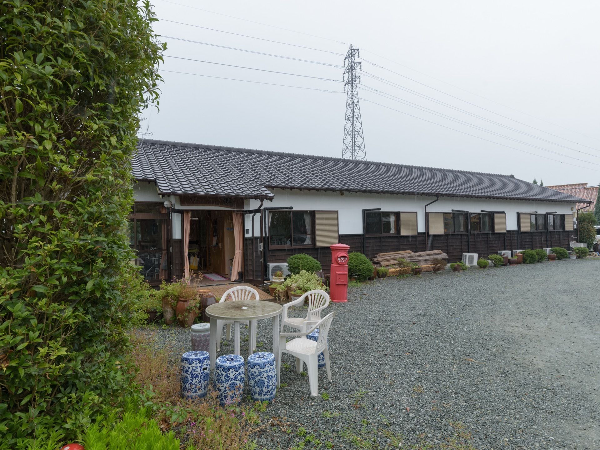 正面に和風の平屋建てのホームが建っている。ホームの左手には緑の木々が植えられていて、近くにテーブルや椅子などが並べられている。
