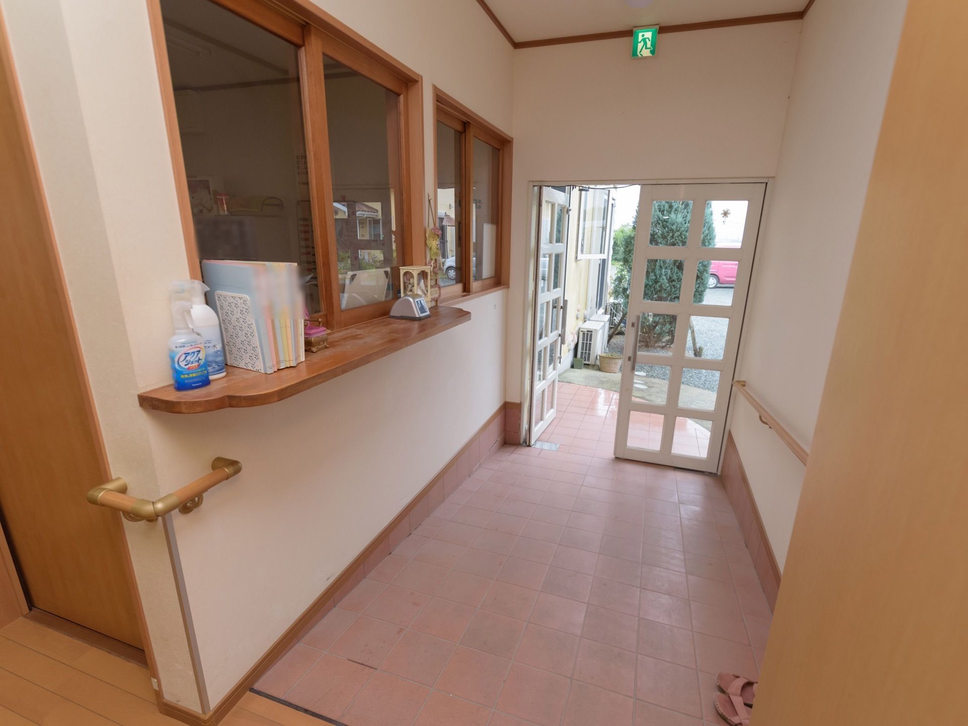 玄関ホールはなだらかなスロープになっている。玄関の周囲の壁には、手すりが設置されていて、玄関の扉からは外の日差しが差し込んでいる。