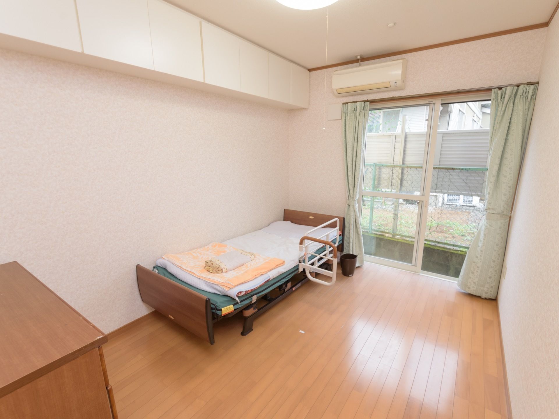 ベッドと収納などが設置された洋風の居室。大きな掃き出しの窓があり、壁にはエアコンが備え付けられている。