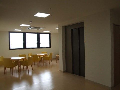 四人掛けの椅子とテーブルが複数配置された窓のある空間である。部屋の中央にはエレベーターが設置されている。