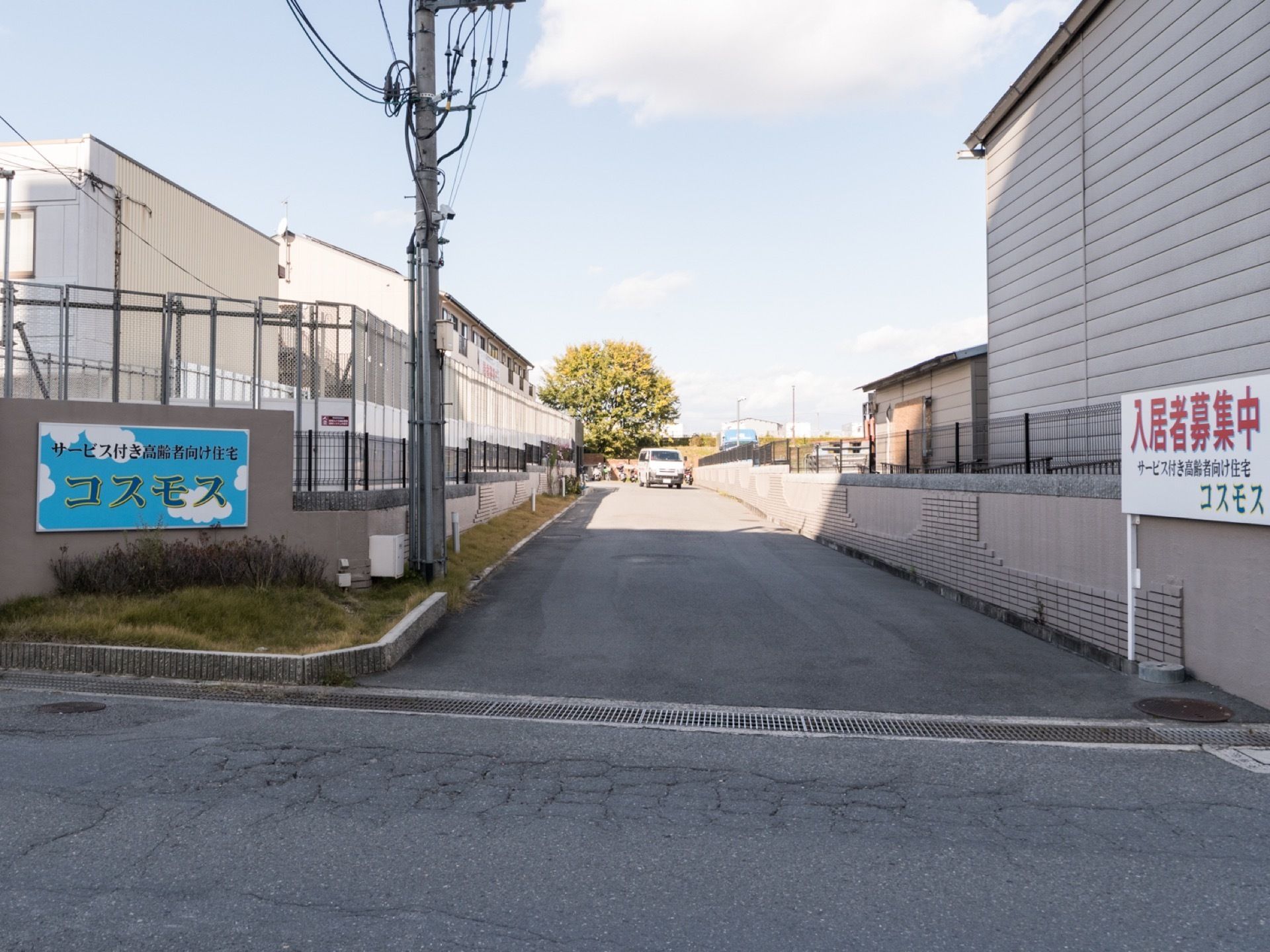 施設名が書かれたプレートが掲示されている。入居者募集中の看板が立てられている。自動車が１台停まっている。