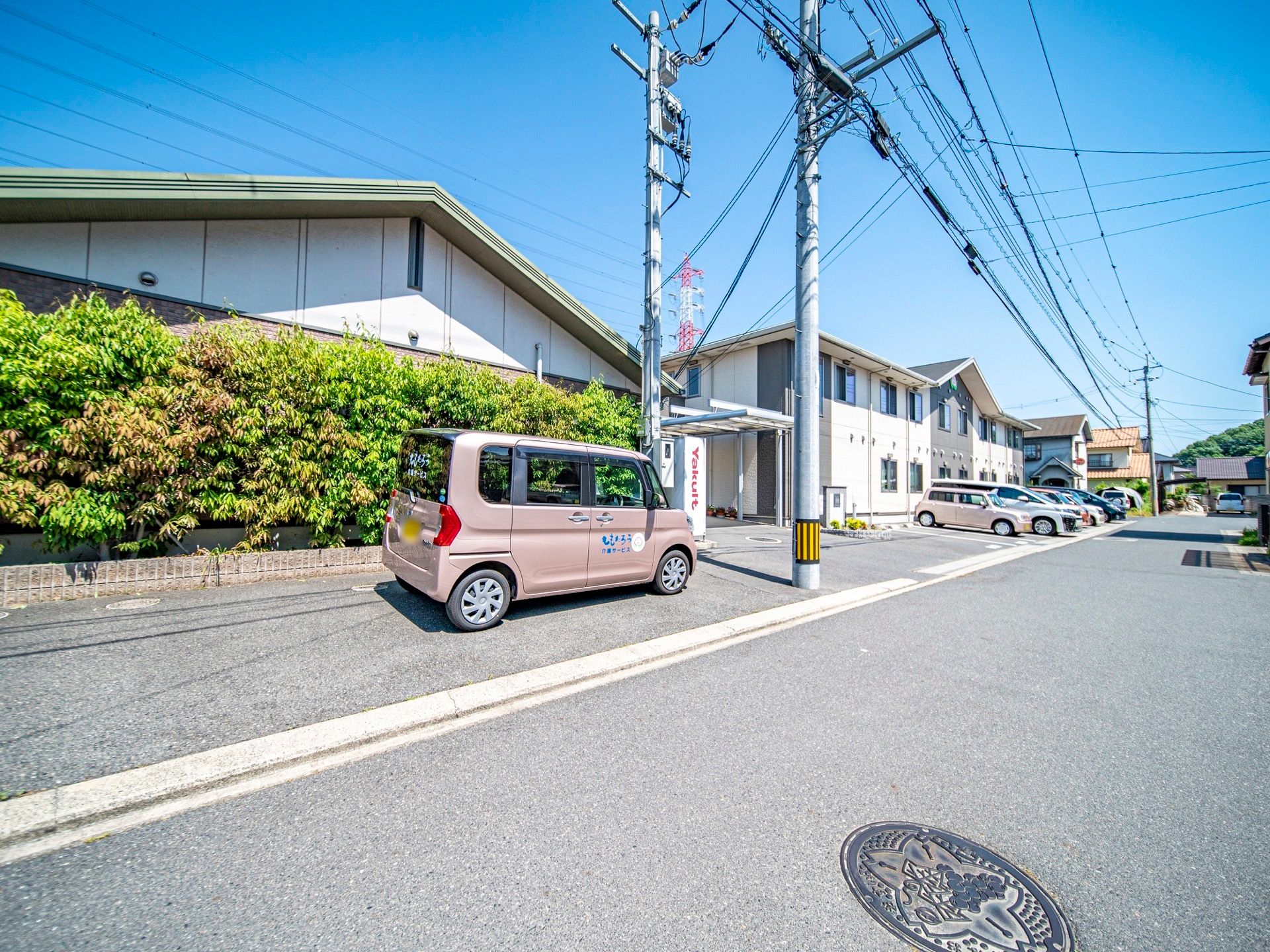 緑の屋根が特徴の平屋建ての施設である。敷地は生垣で囲まれており、側に送迎車が停められている。自販機が設置されている。