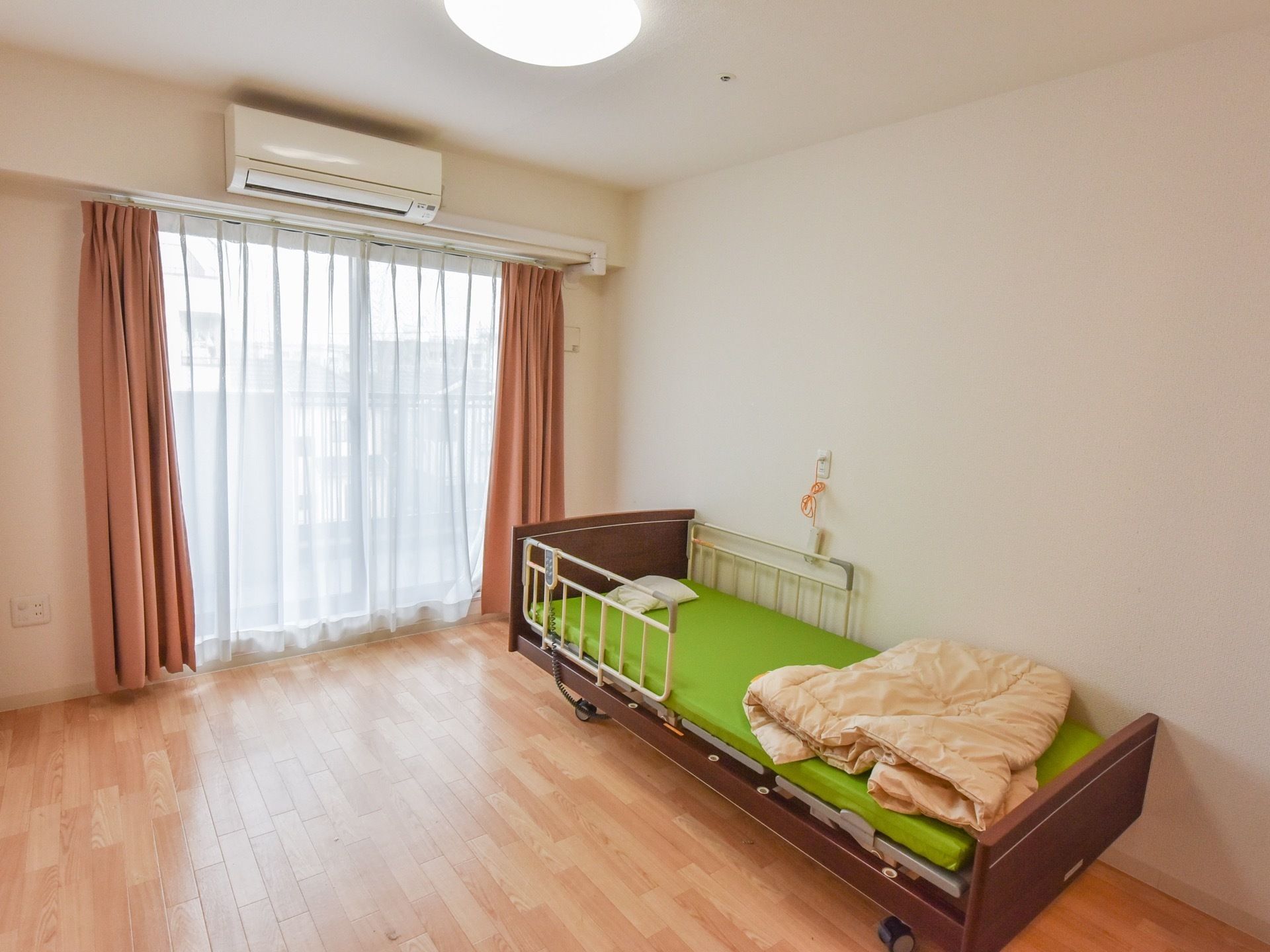 居室の右端には、電動ベッドが設置されている。鮮やかな黄緑色のマットの上に、小さい枕と掛け布団が置いてある。