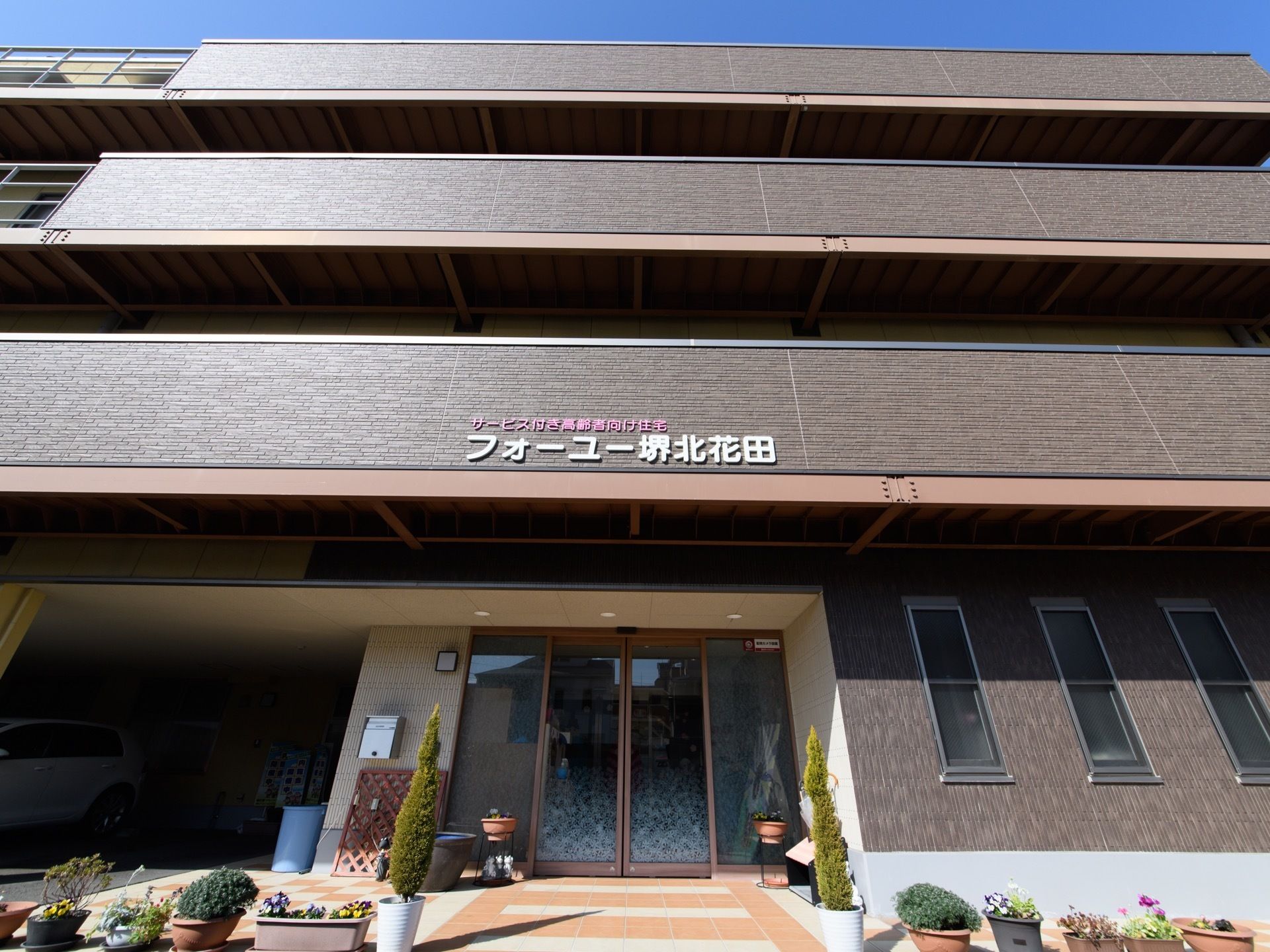 エントランスには、たくさんのプランターが置かれている。また隣には屋根のついた、駐車スペースを用意している。