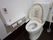 白を基調とした清潔感のある個室トイレである。温水洗浄機能付きの便座となっており、壁には手すりや呼び出しボタンが設置されている。