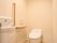 手洗い場とタンクレス温水洗浄便座のあるトイレである。木目調のペーパーホルダーと手すりも設置されている。