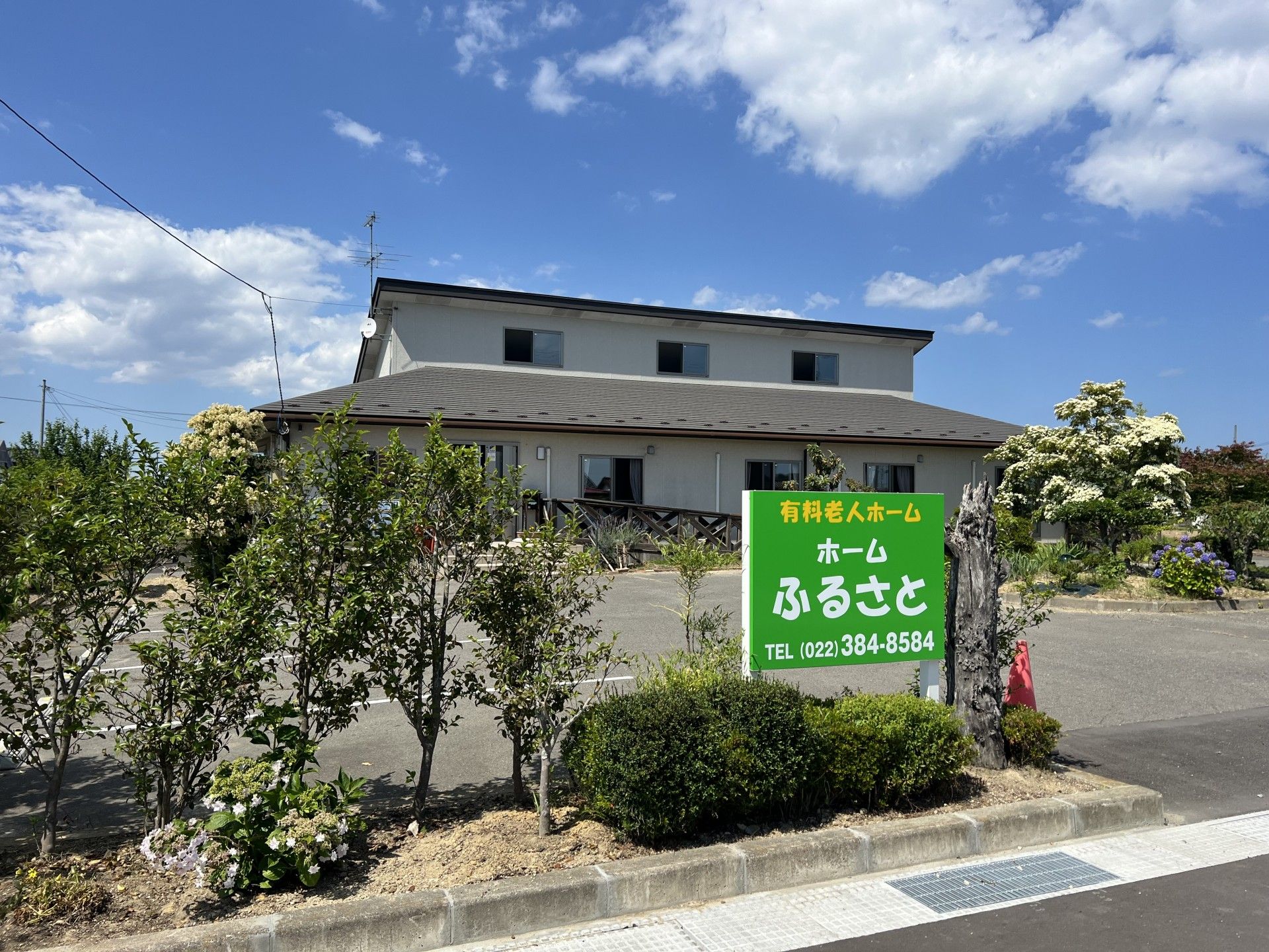 「ホームふるさと」の外観。緑豊かな環境のもと、白の外壁と黒の屋根の平野建ての施設である。