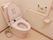 居室のトイレはピンク色のウォシュレット水洗トイレ。壁にはL字型の手すりとスイッチ類、ペーパーが設置されている。