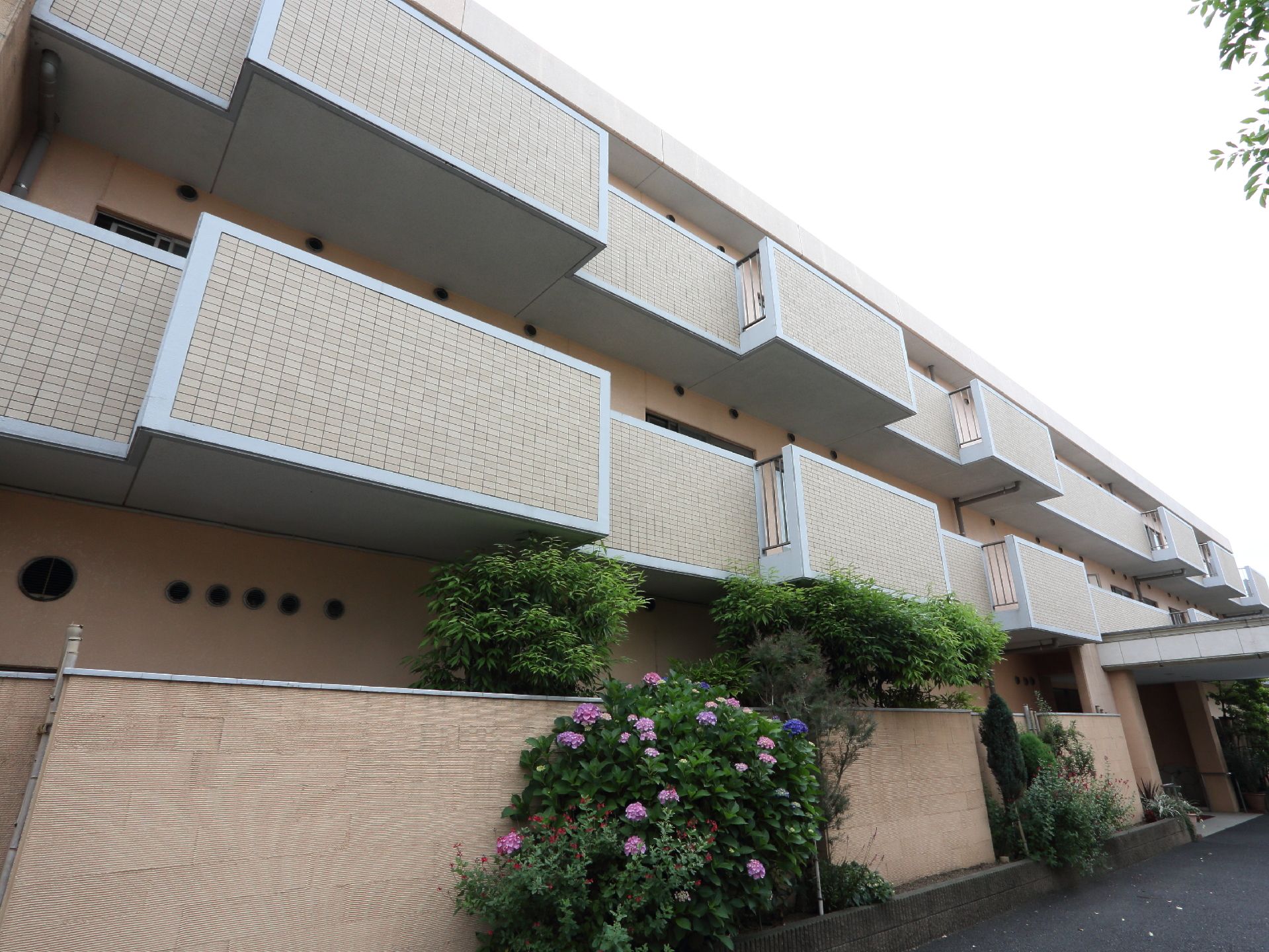 オレンジ系のおしゃれな3階建ての建物。各居室にはテラスが設置されている。1階には庭があり緑がたくさんある。