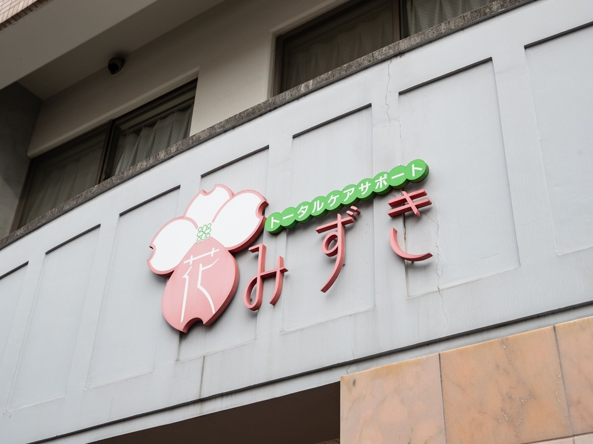 居室には掃き出し窓とベランダが備わっている。ベランダの柵の外側に、パステルカラーの施設名とマークが目立つように大きく記されている。