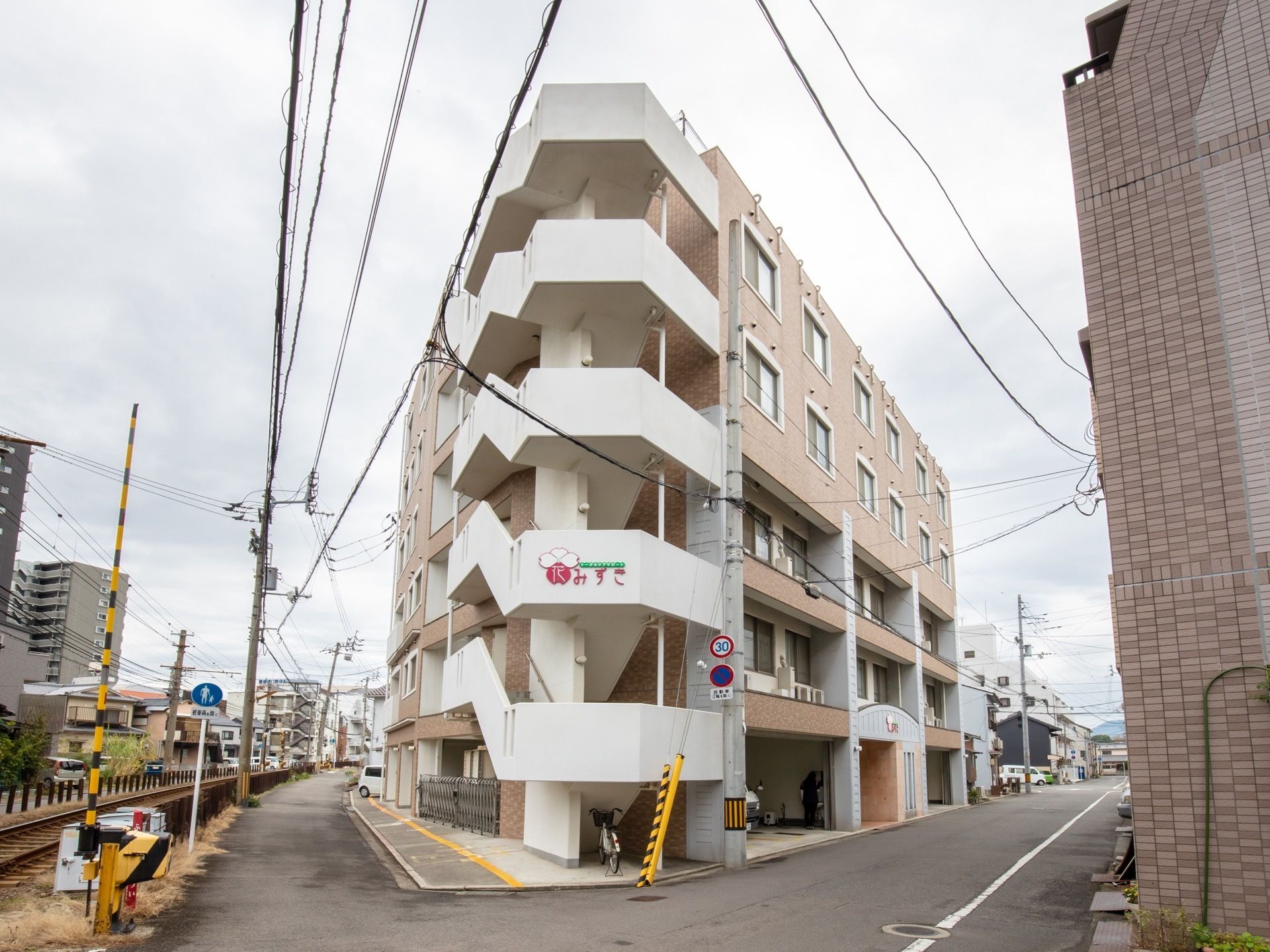 柔らかい色調の５階建て施設の外観である。住宅地に建っており、お車ではもちろんのこと、公共交通でも来訪していただきやすい場所である。