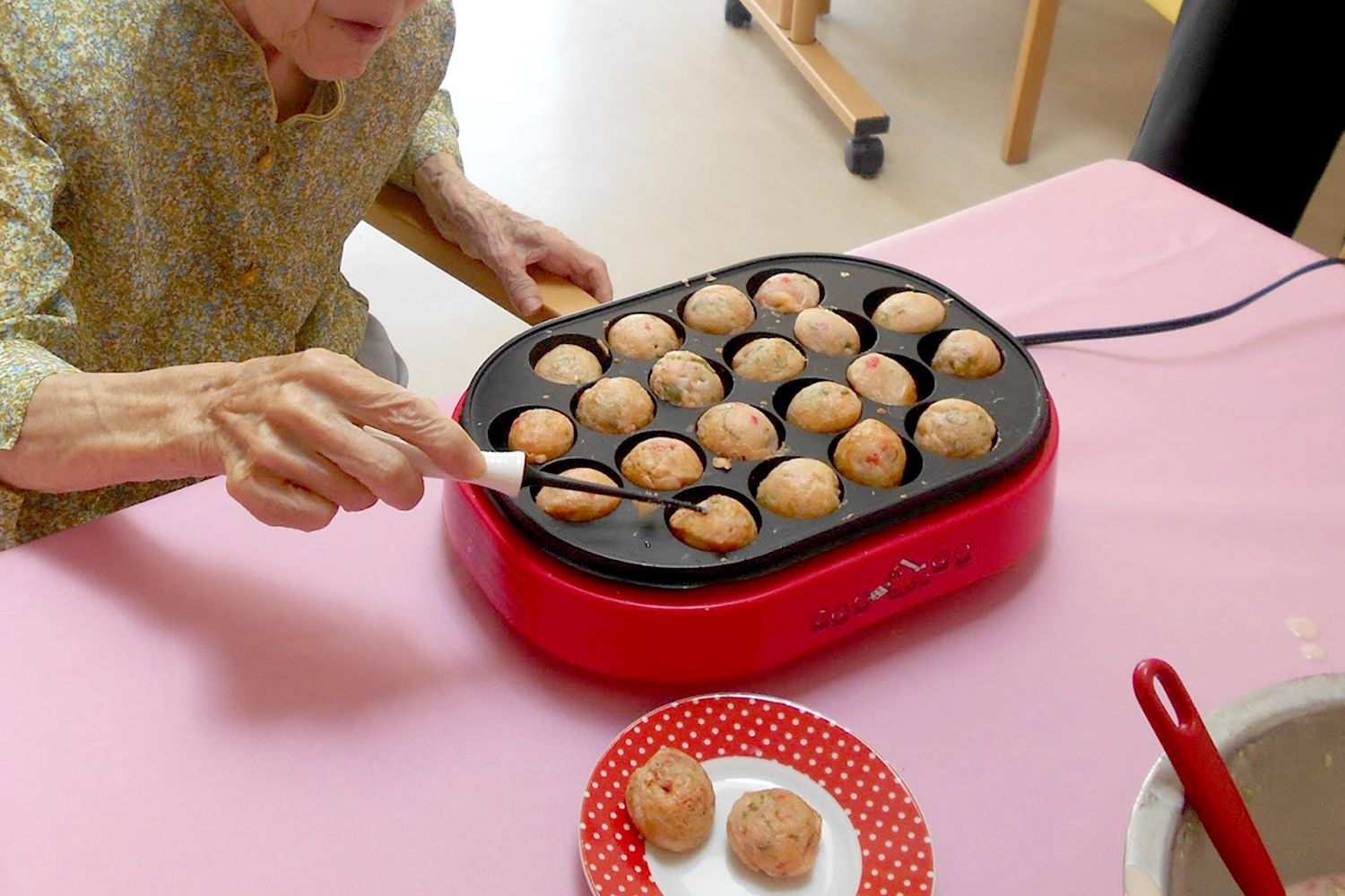 たこ焼き器でたこ焼きを焼く高齢女性