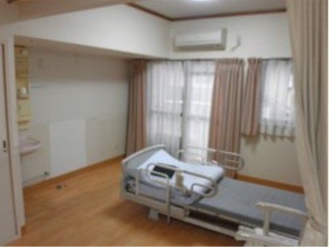 窓にピンクのカーテンがかかった介護用ベッドの置かれた洋室