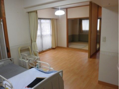 介護用ベッド、ポータブルトイレが置かれ、広々とした洋室
