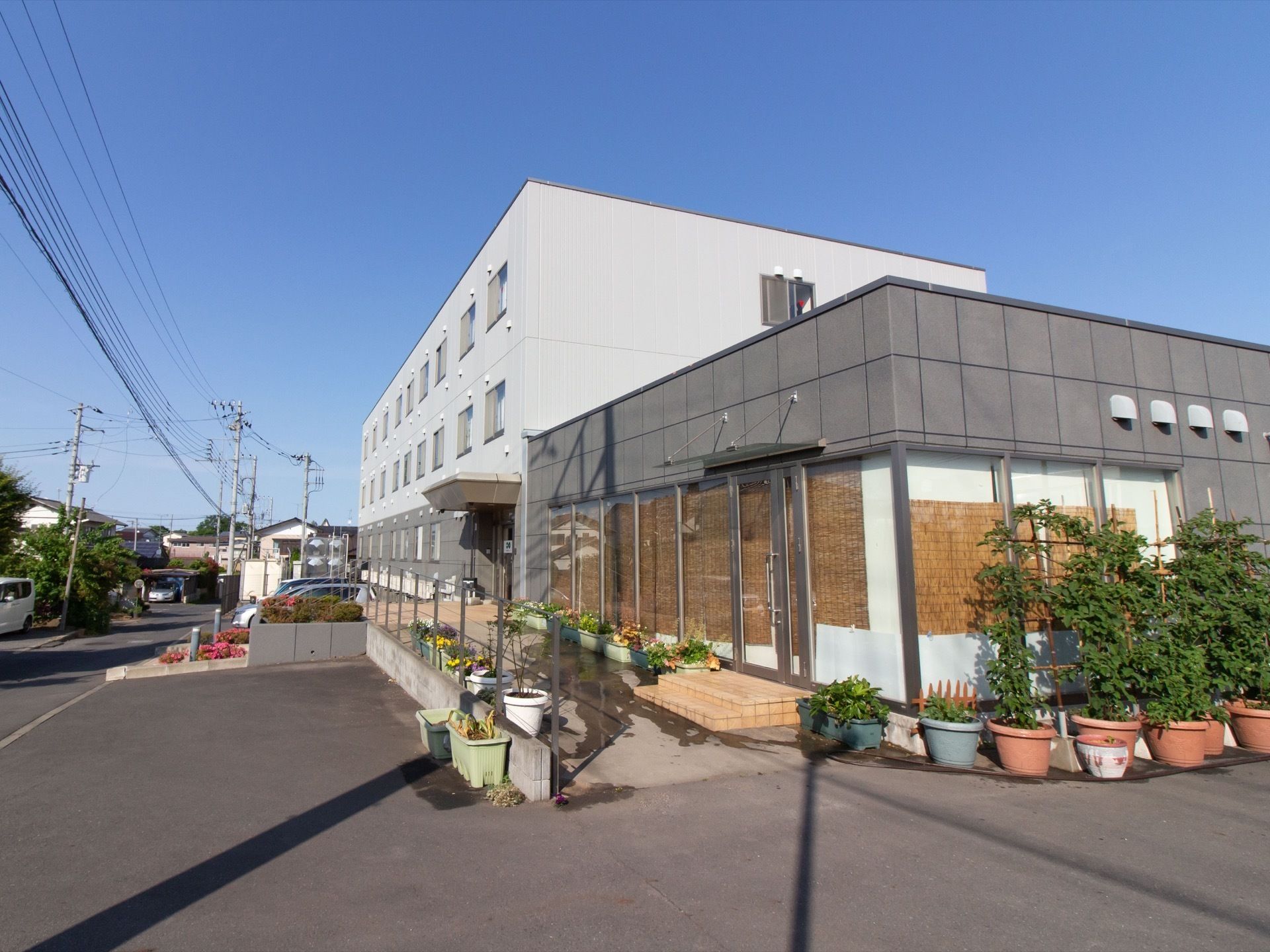 施設は鉄骨造３階建ての建物で、外観は白とグレーのツートンカラーである。道路に面して駐車スペースがある。