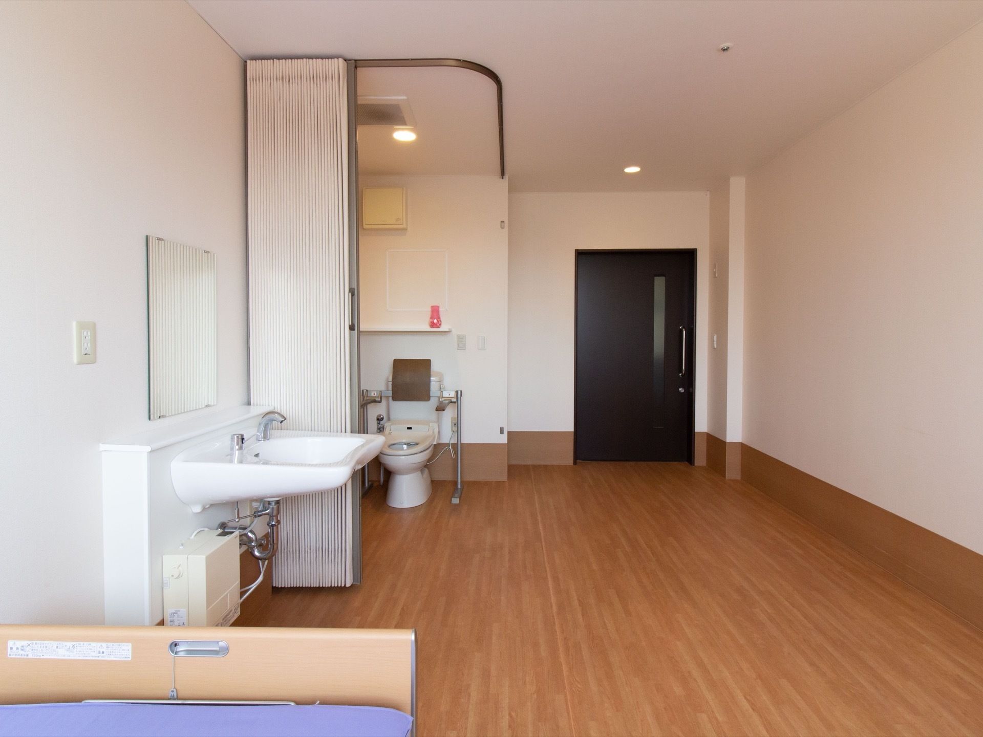 居室の扉はスライド式である。居室に入って右手に洋式トイレがある。鏡の付いた洗面台は、センサーで水が出るタイプの蛇口が付いている。