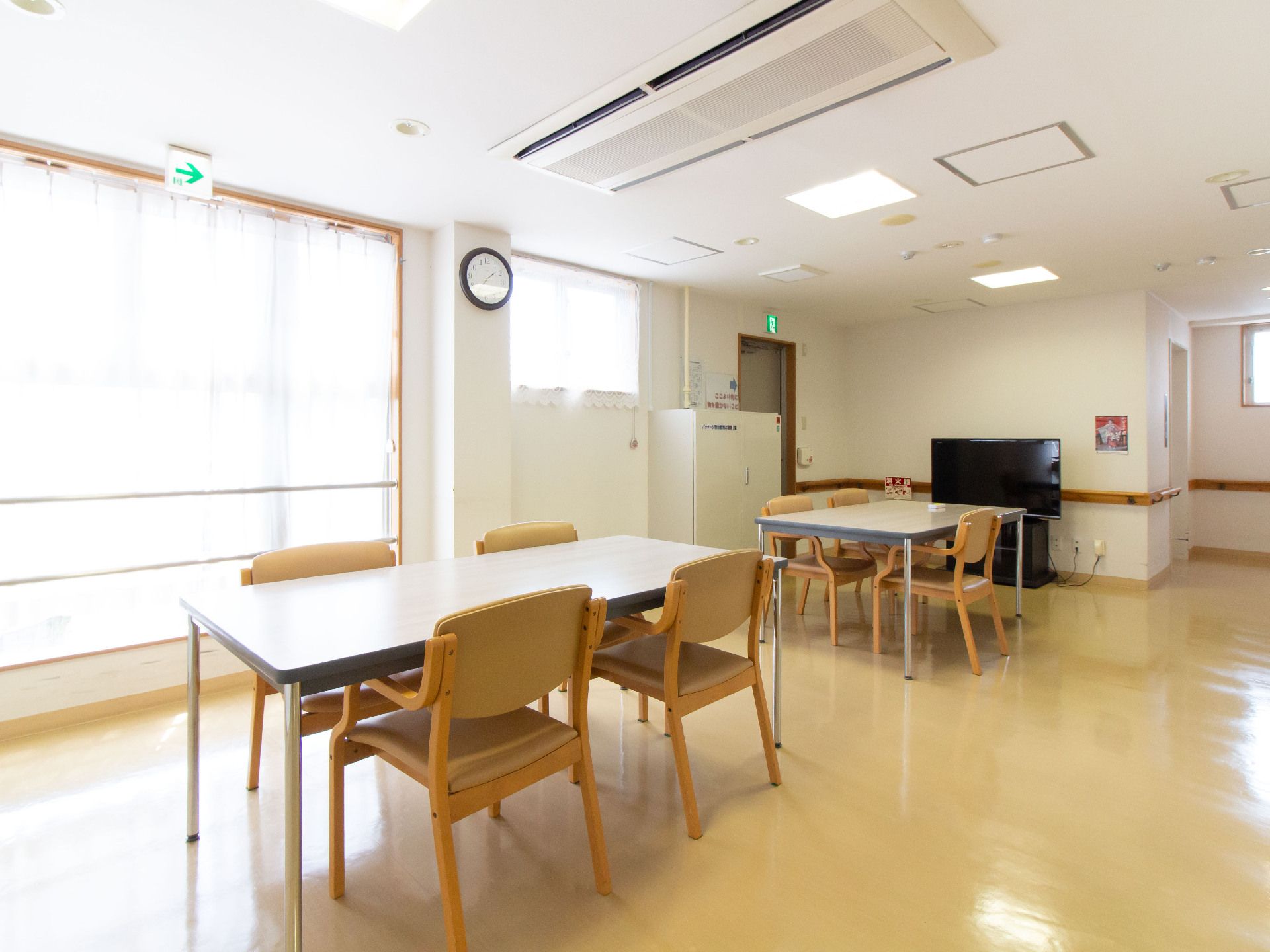 ４人掛けの広いテーブル2つと椅子、テレビの置かれた広い窓のある部屋
