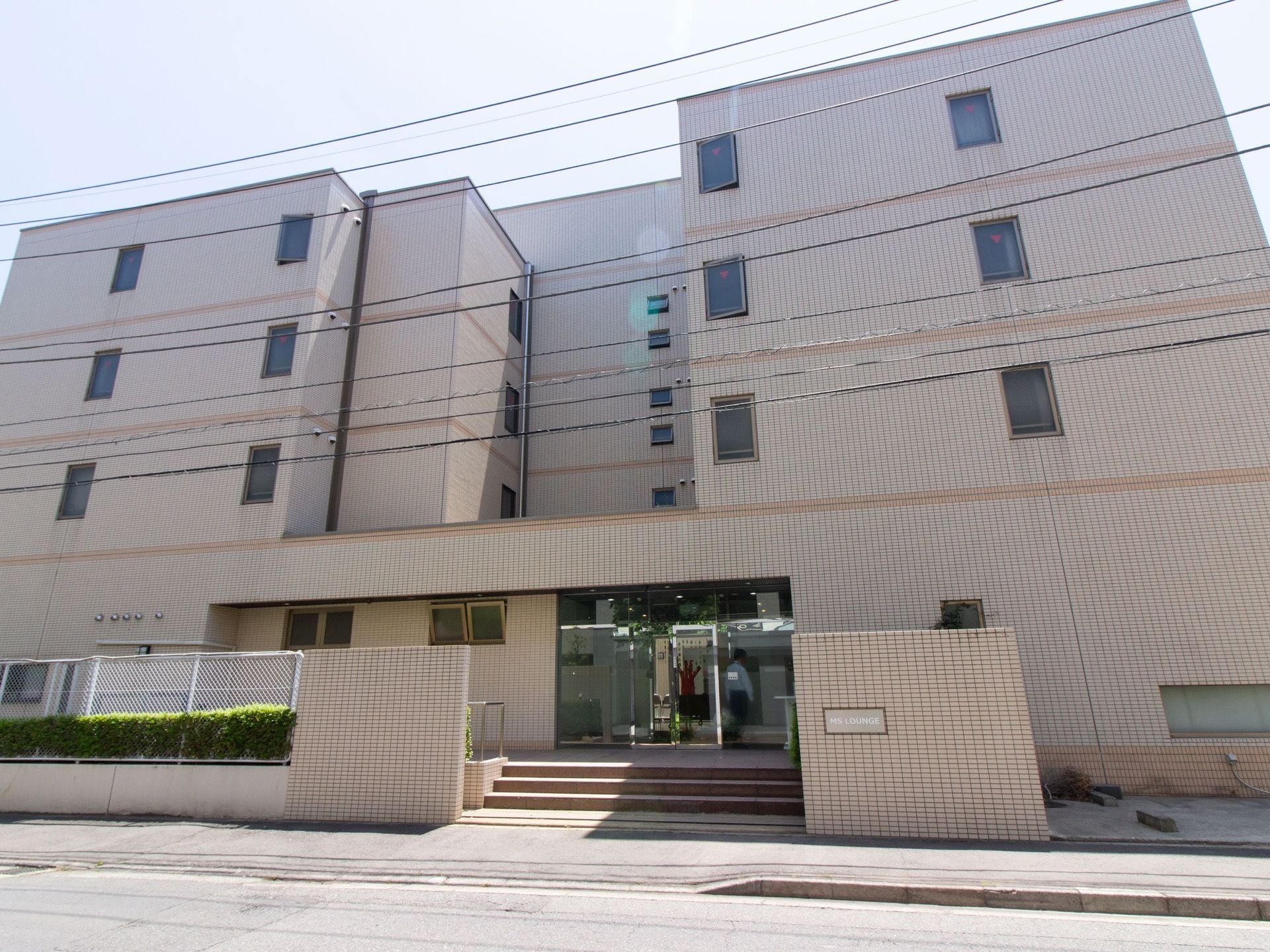 ４階建てのベージュ色の外壁で、落ち着いた雰囲気の建物である。入口のドアはガラス製で内部の様子が一部伺える。