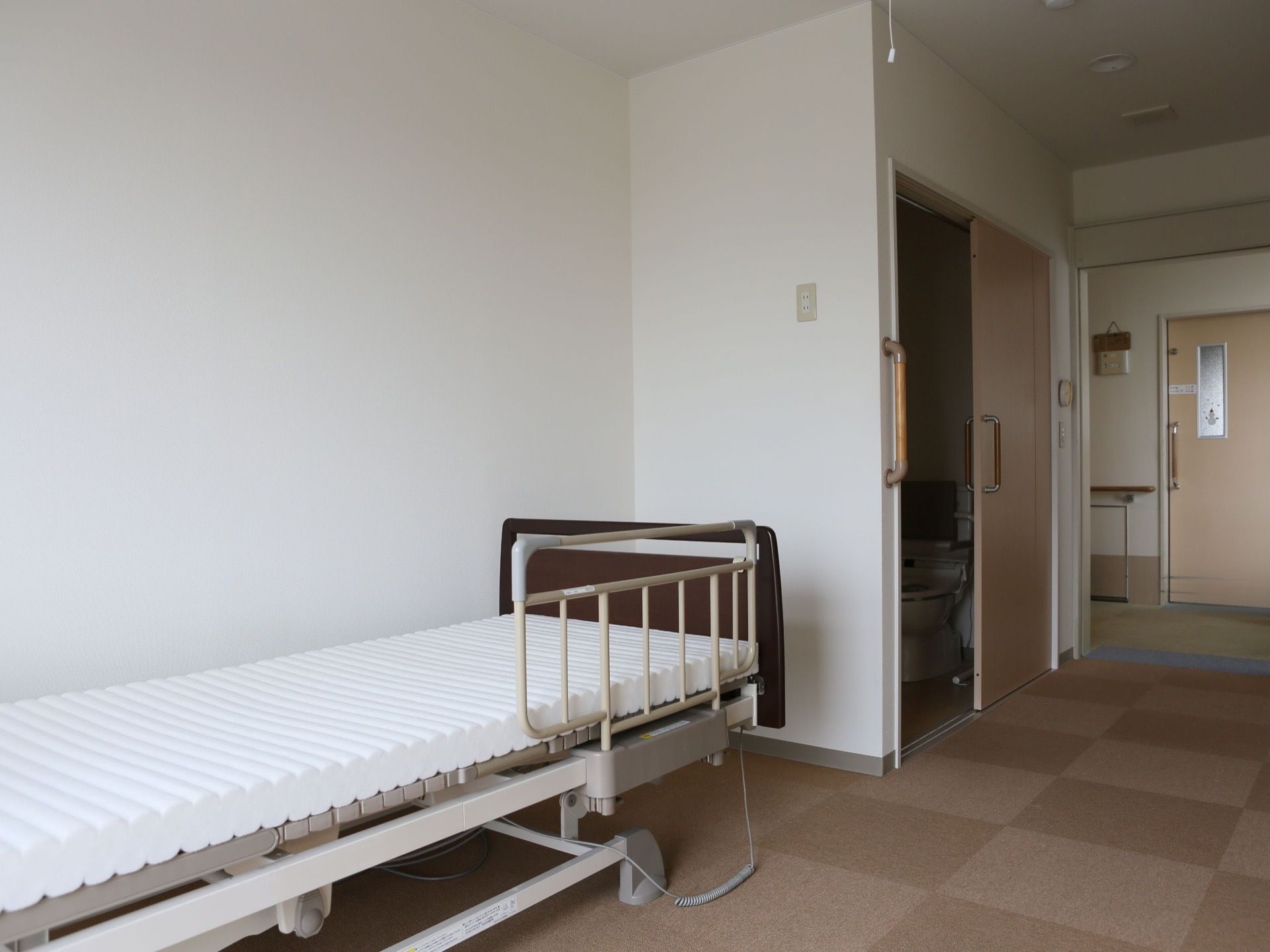 居室に介護ベッドが置かれている。居室内にはトイレがあり、入口には手すりが設けられている。扉は引き戸で、床には段差がない。