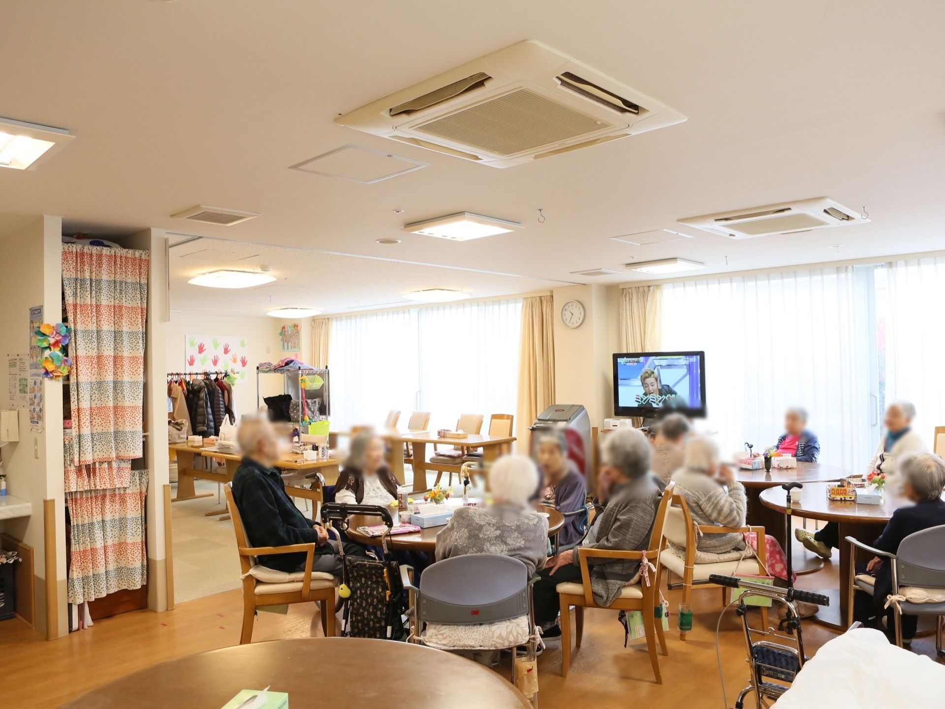 ダイニングの一角に入居者様が集まり、歓談をしたり、テレビを見たりして過ごしている。天井にはビルトインエアコンが設置されている。