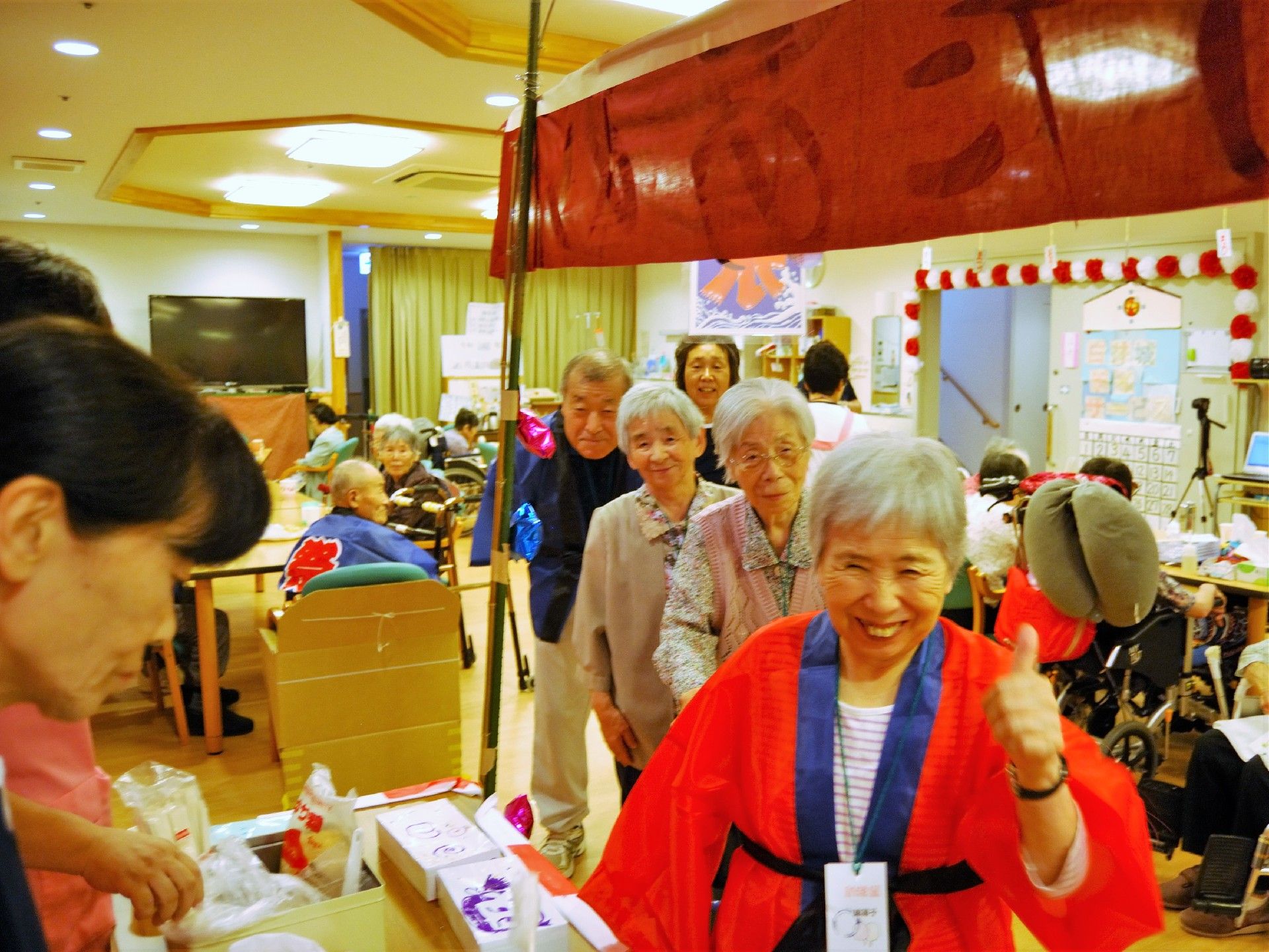 施設内のお祭り広場に法被を着て笑顔で訪れる入居者たち