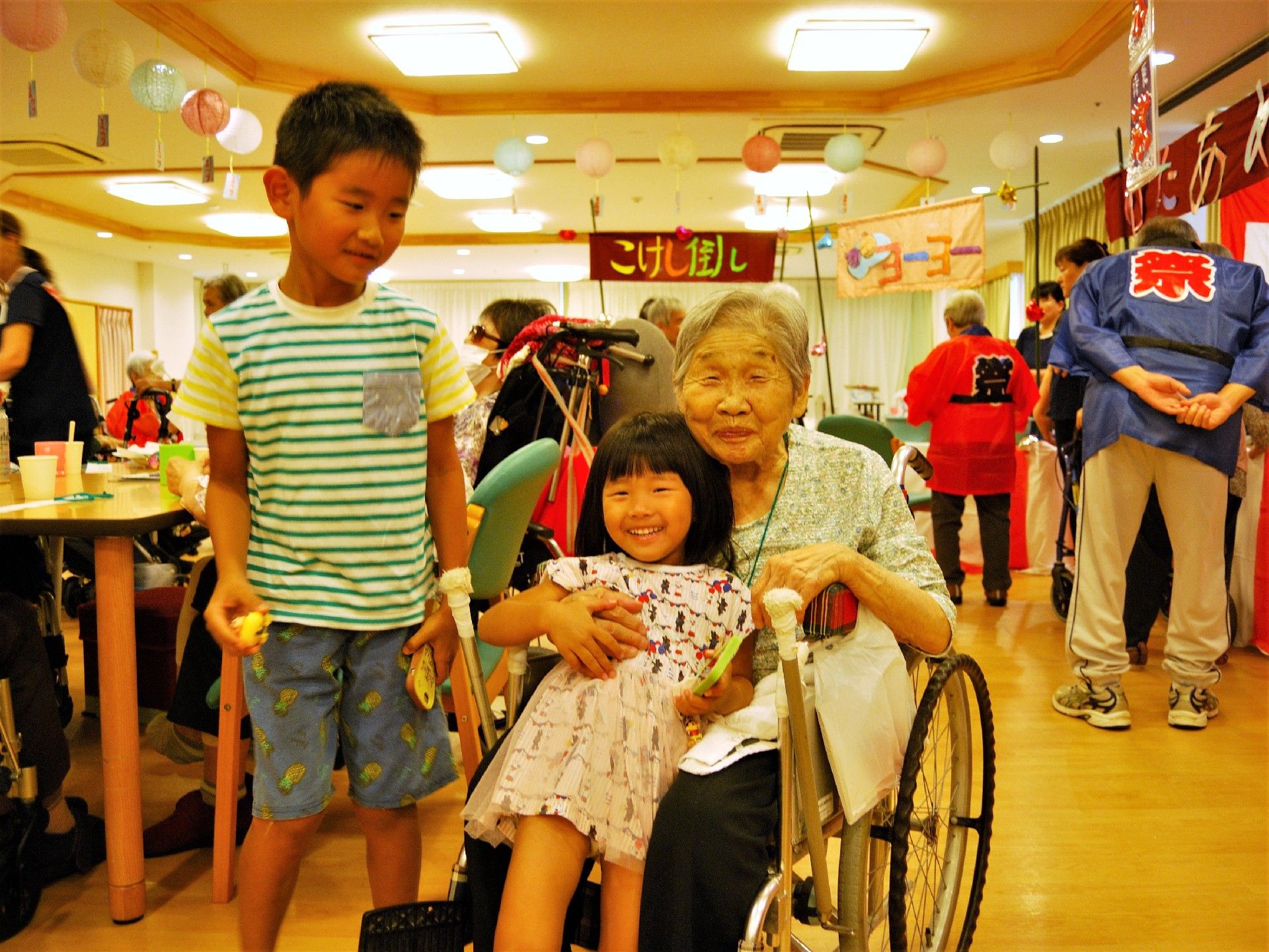 お祭り広場で、子供二人と嬉しそうに微笑んでいる車椅子に乗った女性