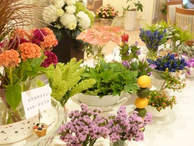 さまざまな植物や花が花瓶に飾られている、白い布がかかったテーブル