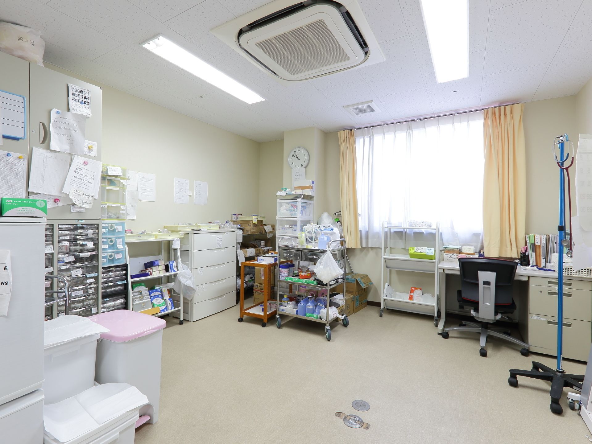 室内に、事務机や書類棚、聴診器など医療関係の道具などが置かれている。冷蔵庫やダストボックスも見える。